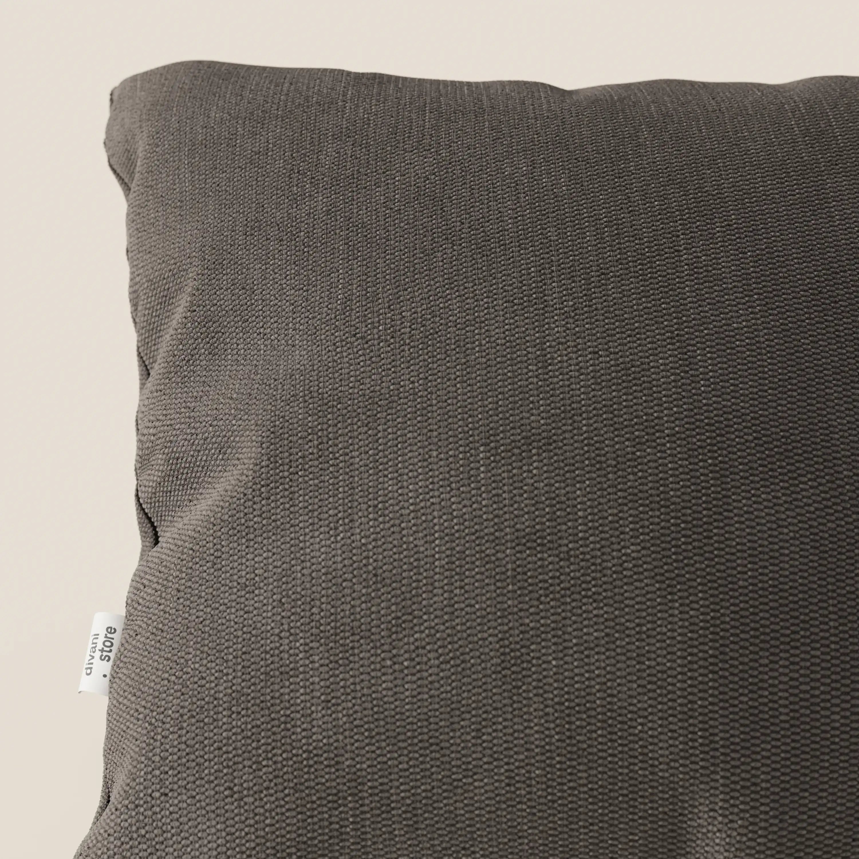 Un primo piano del cuscino Miami 45x45 cm di Divani.Store in T14 marrone mostra il suo tessuto morbido e resistente all'acqua e la sua sottile trama. Una piccola etichetta bianca con testo nero è visibile sulla cucitura sinistra su uno sfondo beige.