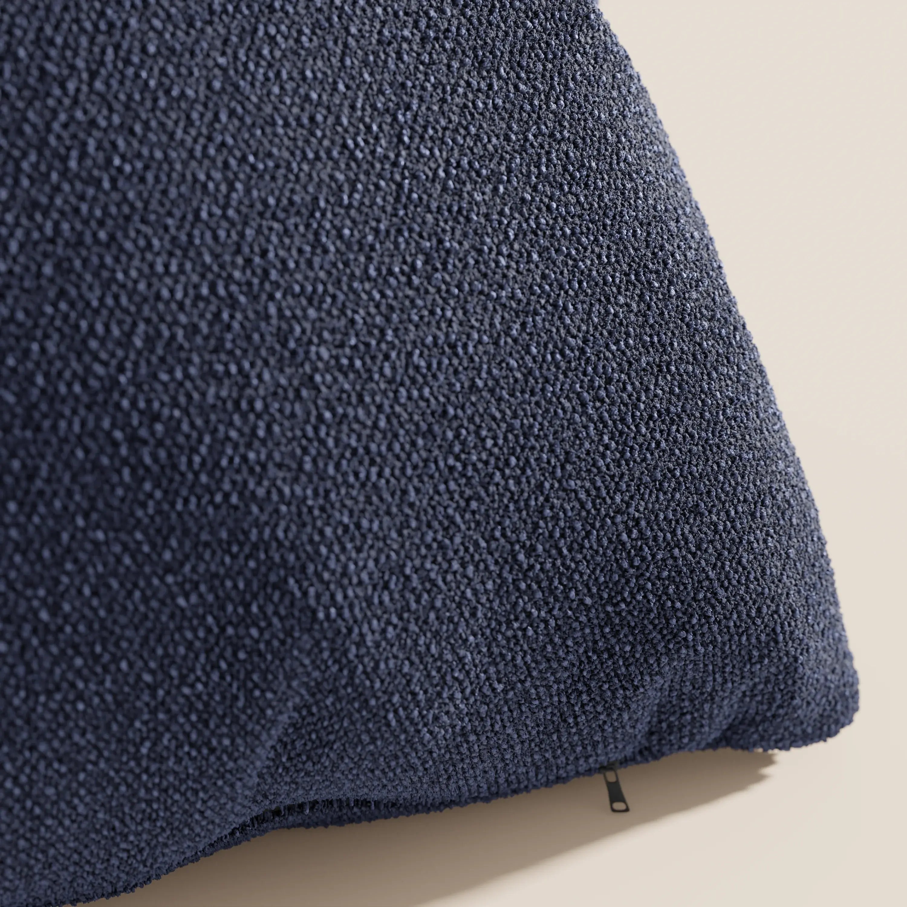 Primo piano del cuscino Lambada di Divani.Store in blu navy, caratterizzato da un tessuto T33 testurizzato, smacchiabile e impermeabile, con un piccolo tiretto nero in corrispondenza della cucitura, su uno sfondo beige chiaro.