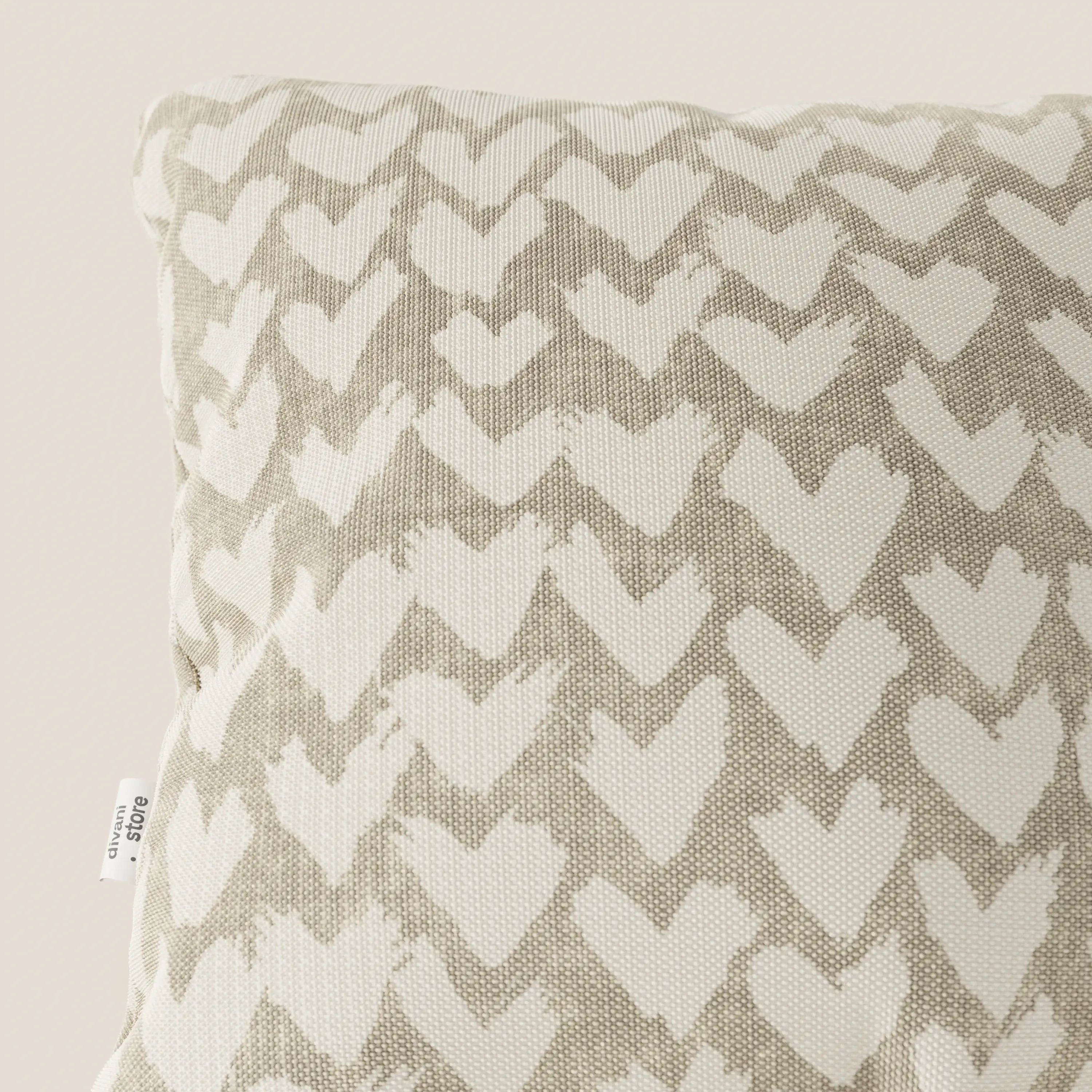 Primo piano dei cuscini geometrici Divani.Store Arrow in beige, caratterizzati da un tessuto strutturato e idrorepellente con un motivo geometrico a cuore. Una piccola etichetta bianca con testo nero appare sul bordo sinistro su uno sfondo beige chiaro.