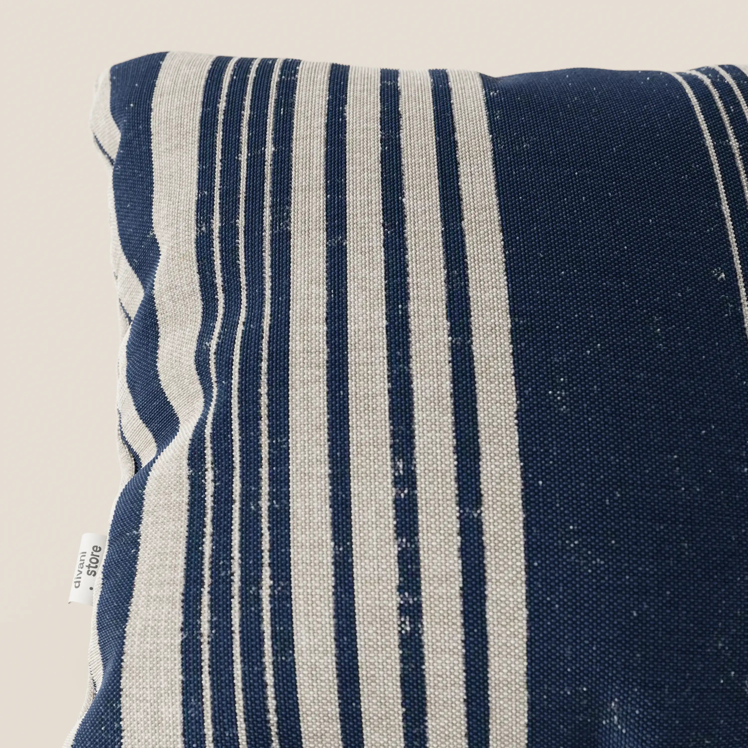 Primo piano del cuscino a fantasia rigata 45x45 di Divani.Store Line in tessuto impermeabile, blu navy a righe verticali beige. Un cartellino bianco indica "100% cotone". Lo sfondo chiaro evidenzia il motivo decorativo e la trama.