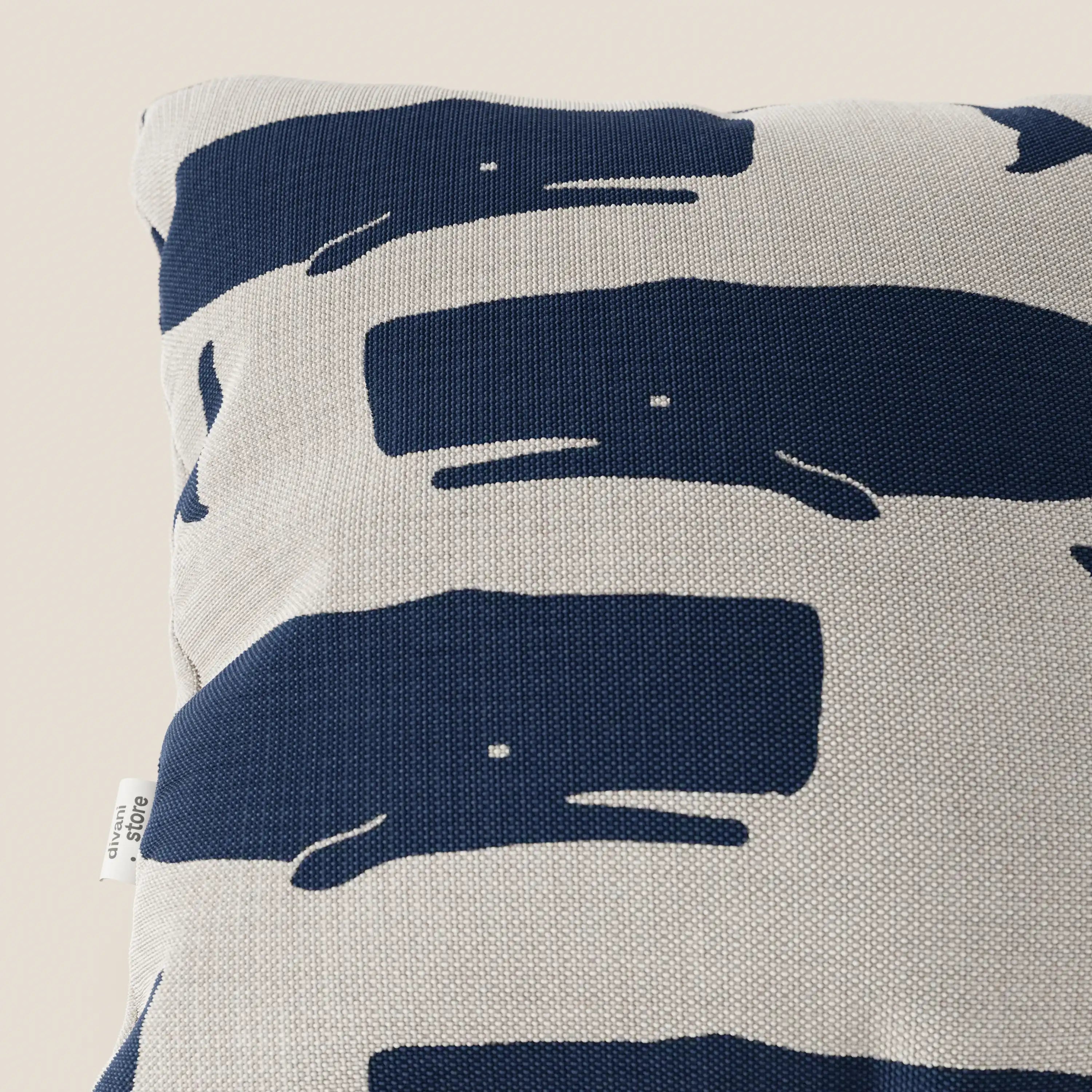 Cuscino quadrato della collezione di cuscini Nautilus di Divani.Store, caratterizzato da balene astratte di colore blu navy con piccoli occhi bianchi su tessuto impermeabile grigio chiaro e etichetta sul bordo sinistro. Stile marino, ideale per la decorazione.