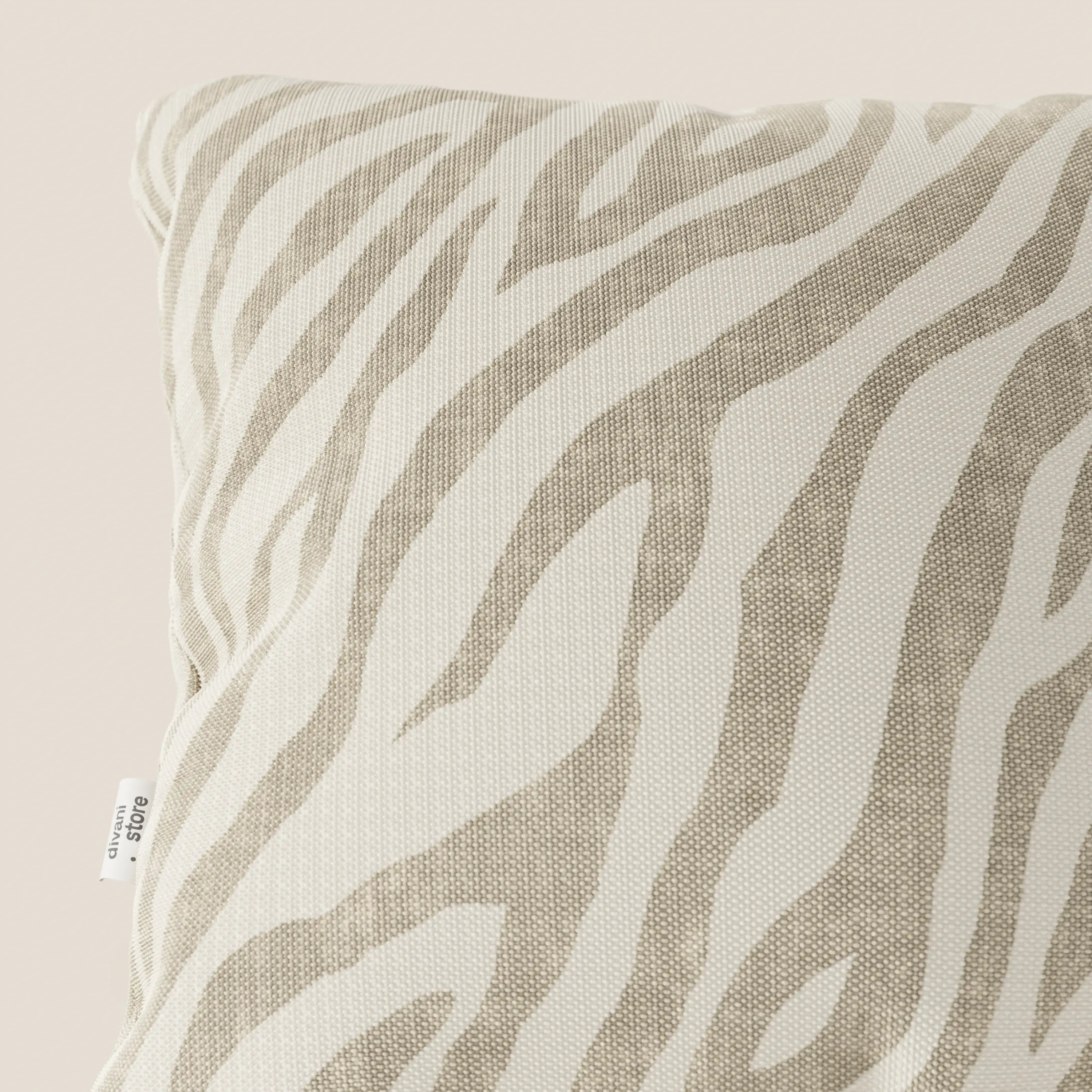 Primo piano di Stripe cuscini geometrici in tessuto Idrorepellente di Divani.Store, a righe zebrate bianche e beige. Una piccola etichetta in tessuto bianco con testo nero è cucita nella cucitura. Lo sfondo è di un colore chiaro e neutro.