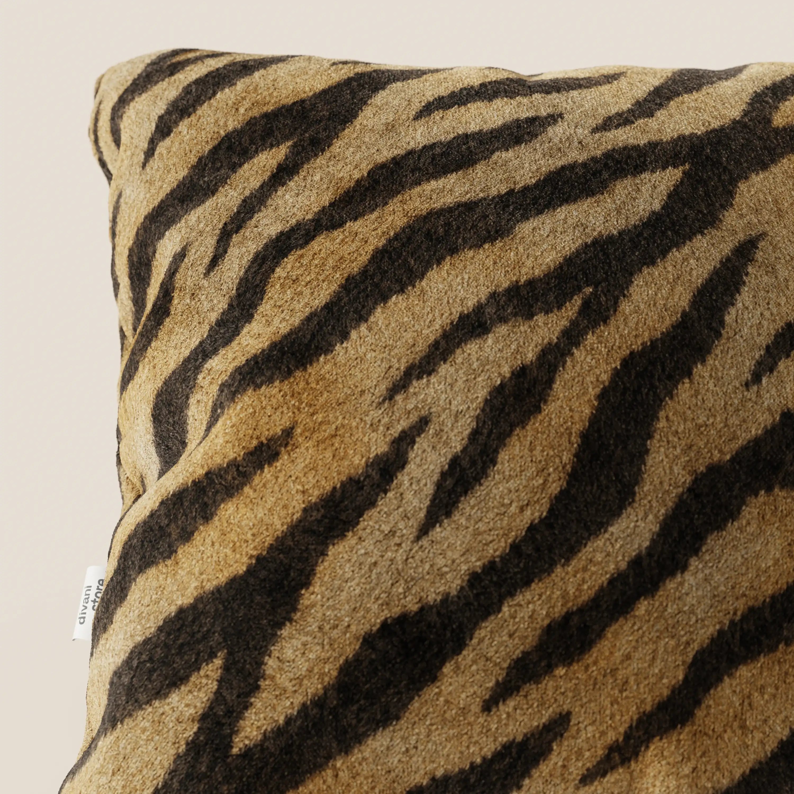 Primo piano del cuscino Wild della collezione Wild di Divani.Store, un cuscino quadrato in microfibra impermeabile con motivo a strisce tigrate marrone, marrone e nero e consistenza morbida. Sul bordo si trova una piccola etichetta bianca; lo sfondo è beige.