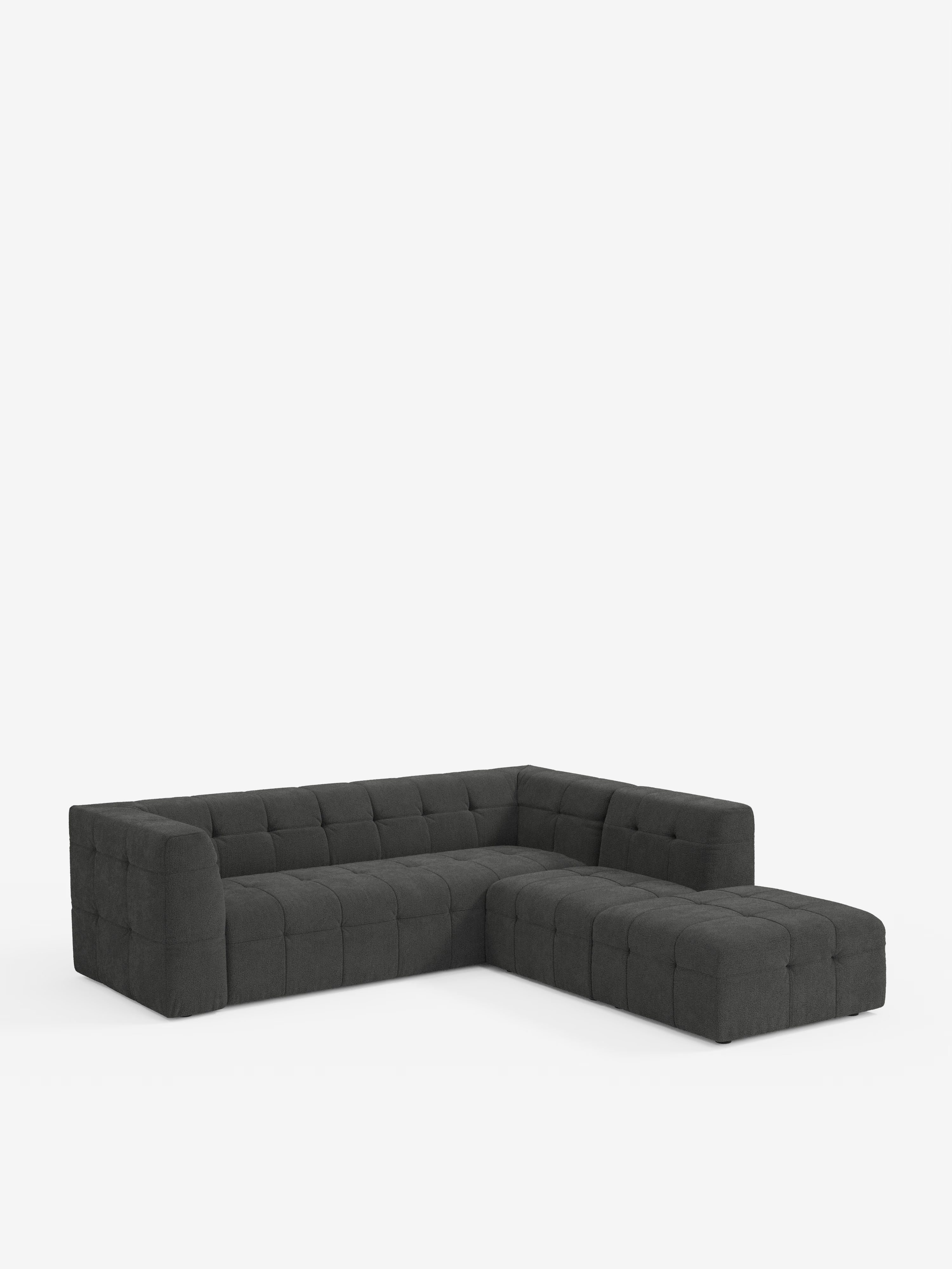 Un divano angolare componibile e modulare della linea Mosaic di Divani.Store, caratterizzato da un rivestimento bouclé capitonné grigio scuro in tessuto smacchiabile T21 e da braccioli bassi e squadrati, presentato su uno sfondo bianco a tinta unita.