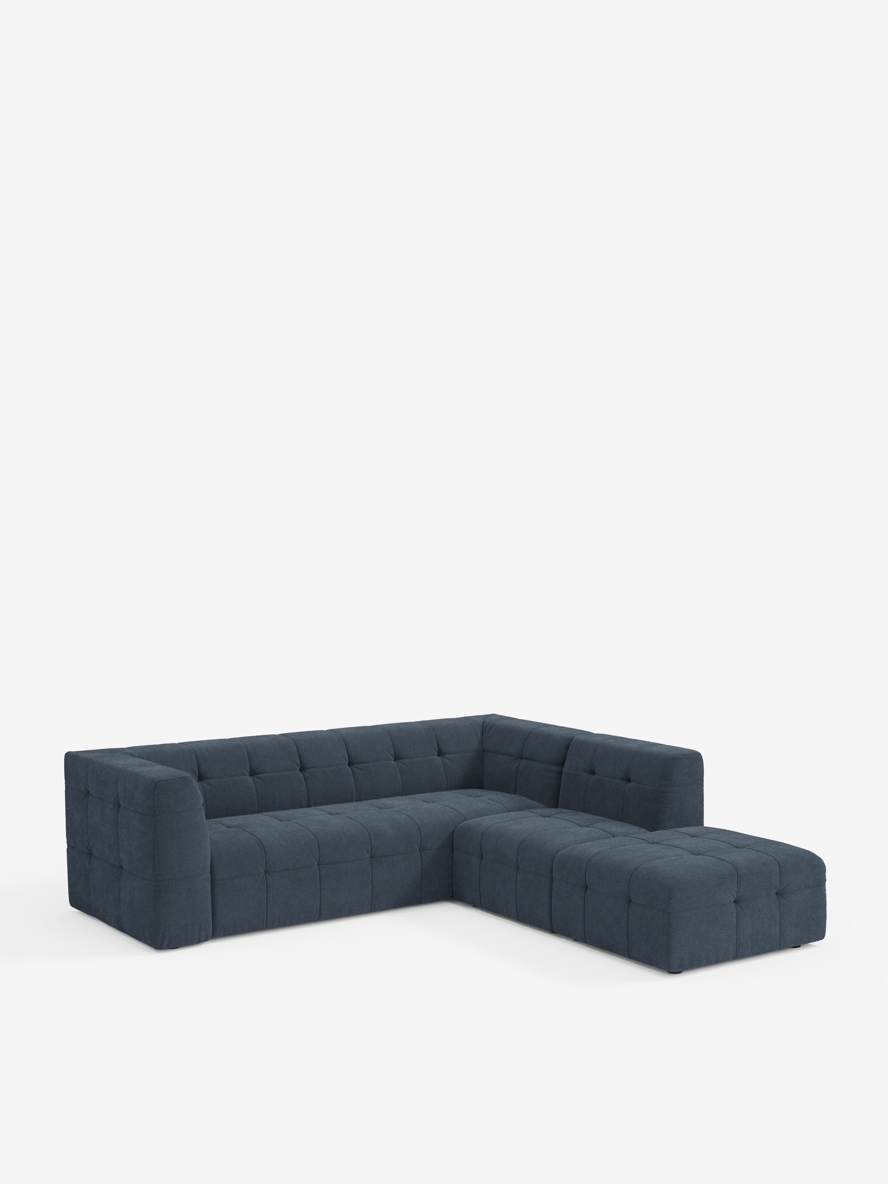 Un divano angolare componibile e modulare Mosaic in bouclé blu scuro di Divani.Store, caratterizzato da cuscini quadrati capitonné e braccioli bassi in lussuoso tessuto T21 antimacchia, è esposto su uno sfondo bianco a tinta unita.