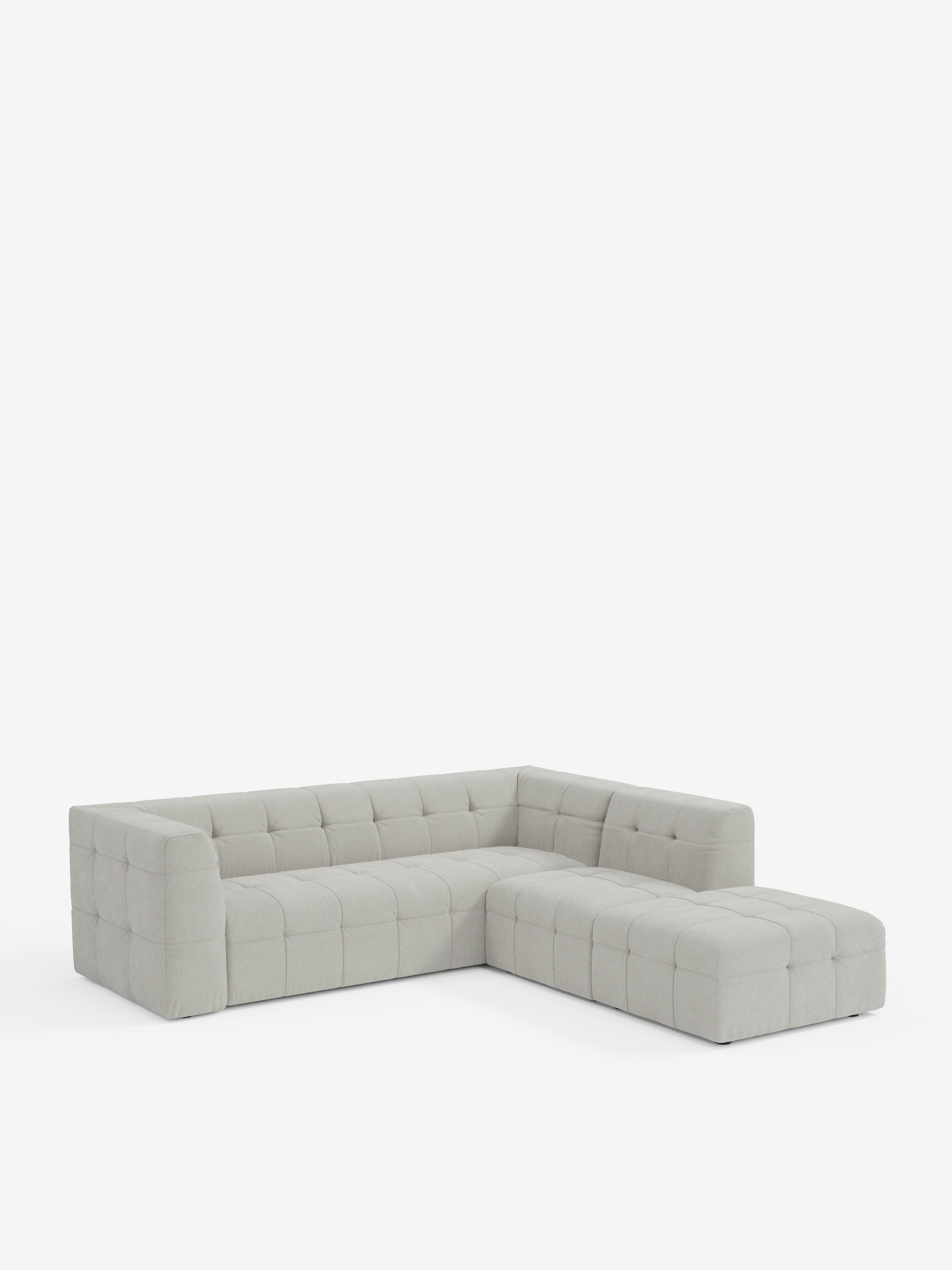 Un moderno divano angolare componibile e modulare della linea Mosaic in bouclé di Divani.Store, realizzato in tessuto T21 grigio chiaro, resistente alle macchie, con rivestimento capitonné (imbottito a ciuffetti) e imbottitura quadrata sia sulla seduta che sullo schienale. Con il suo design minimalista, è perfetto per un soggiorno moderno ed è raffigurato su uno sfondo bianco a tinta unita.