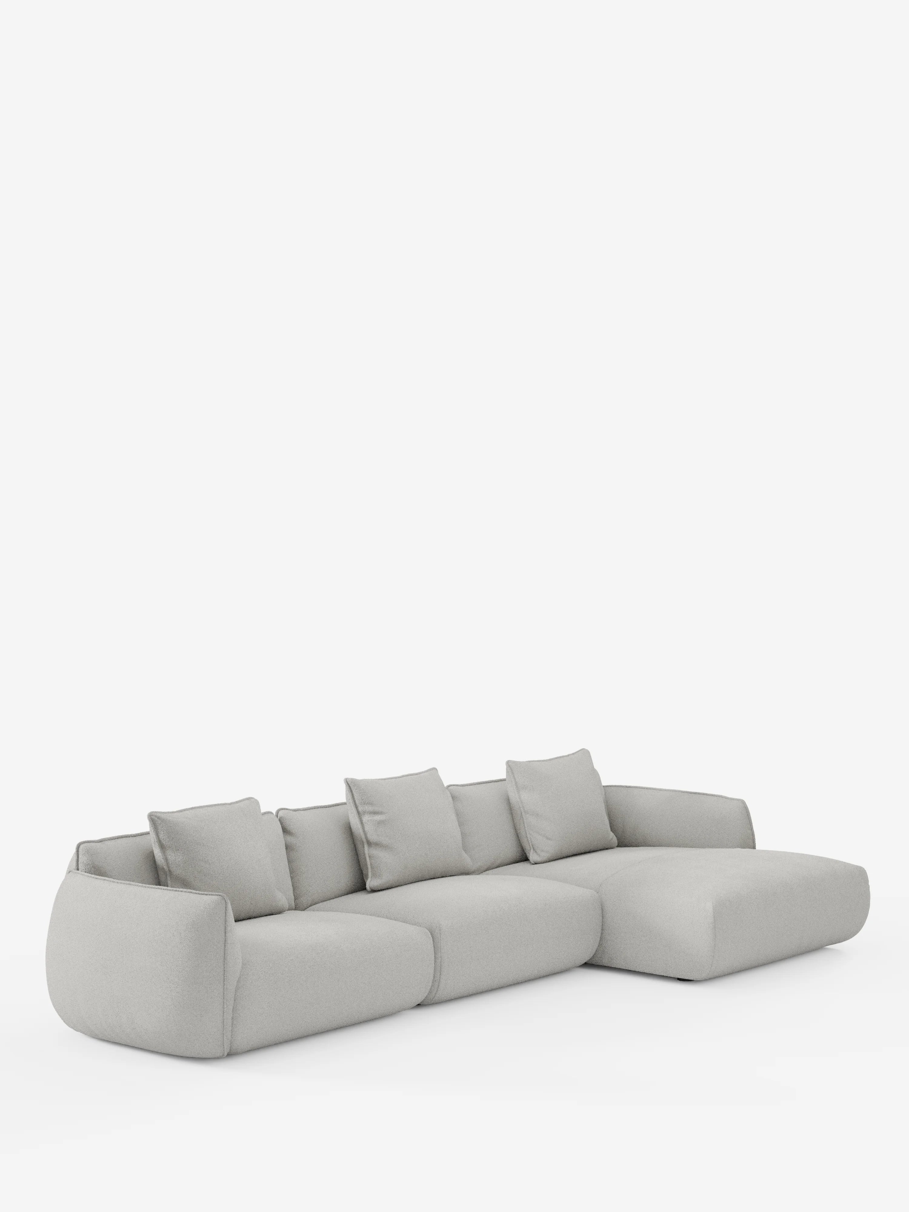 Un moderno divano angolare Nimbus con penisola componibile di Divani.Store, realizzato in tessuto effetto cotone (T33) di colore grigio chiaro, morbido e resistente alle macchie, dotato di quattro cuscini di seduta e cinque cuscini dello schienale coordinati, con bordi delicatamente arrotondati e una chaise longue estesa sul lato destro, su uno sfondo bianco a tinta unita.
