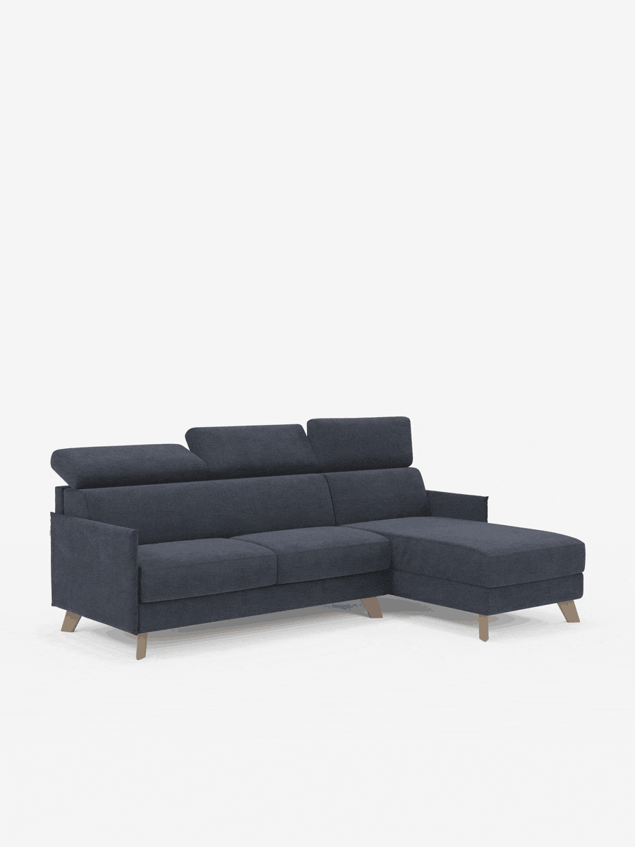 Un divano letto matrimoniale angolare Divani.Store Sole, con penisola contenitore e poggiatesta reclinabili, rivestito in tessuto T23 facile da pulire con tonalità di blu scuro, spicca su uno sfondo bianco a tinta unita. Caratterizzato da gambe in legno, poggiatesta regolabili e una chaise longue sul lato destro, il suo design moderno e minimalista riflette lo stile scandinavo, garantendo al contempo eleganza e funzionalità.