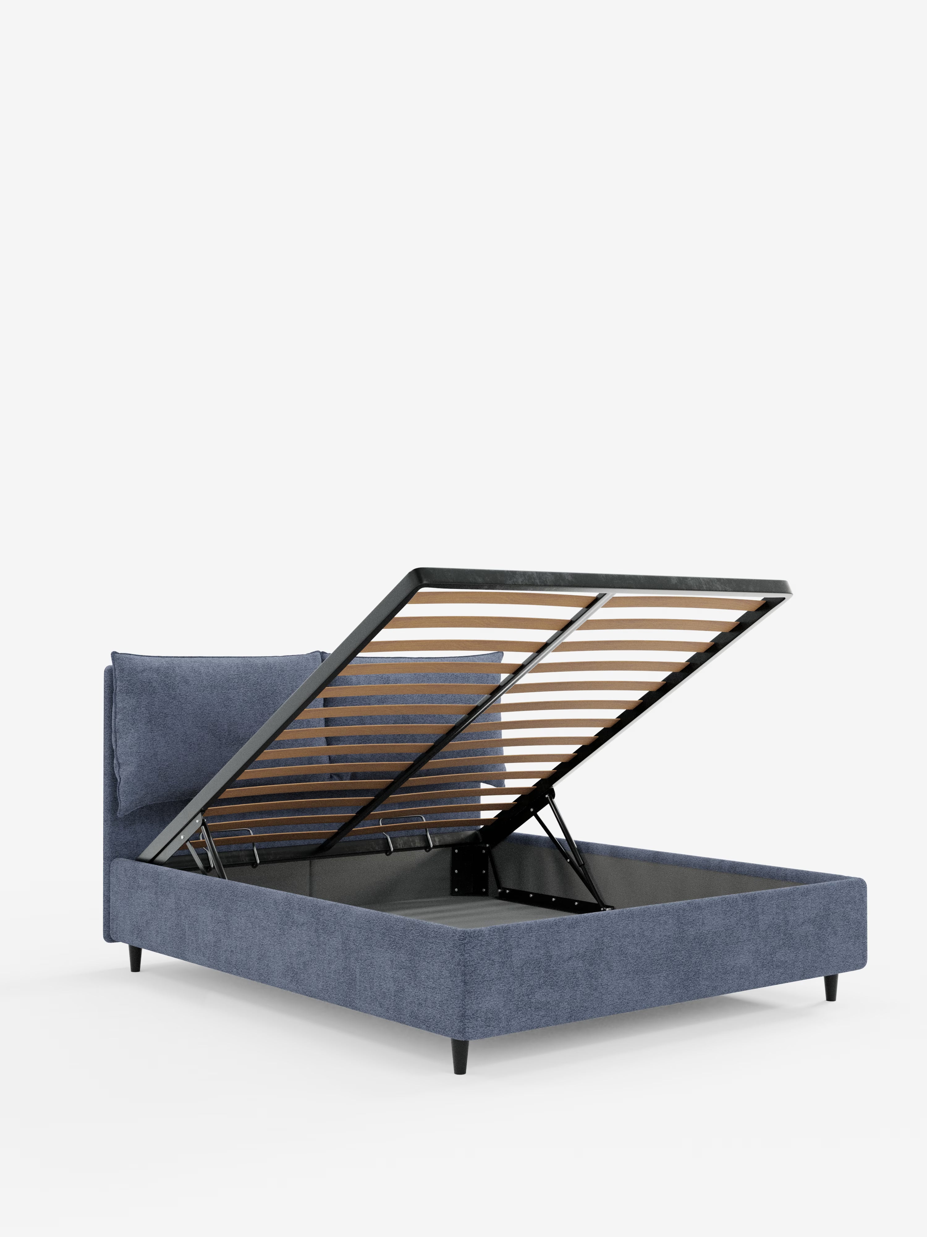 Un letto imbottito blu ZAYRON con contenitore e morbidi cuscini regolabili di Letti.store, caratterizzato da un design moderno in tessuto certificato Oeko-Tex®. La struttura del letto poggia su gambe nere inclinate ed è raffigurata con la rete a doghe sollevata, rivelando un ampio vano contenitore sottostante. La testiera imbottita e regolabile e il meccanismo di sollevamento a vista ne fanno un letto contenitore ideale. Lo sfondo è bianco a tinta unita.