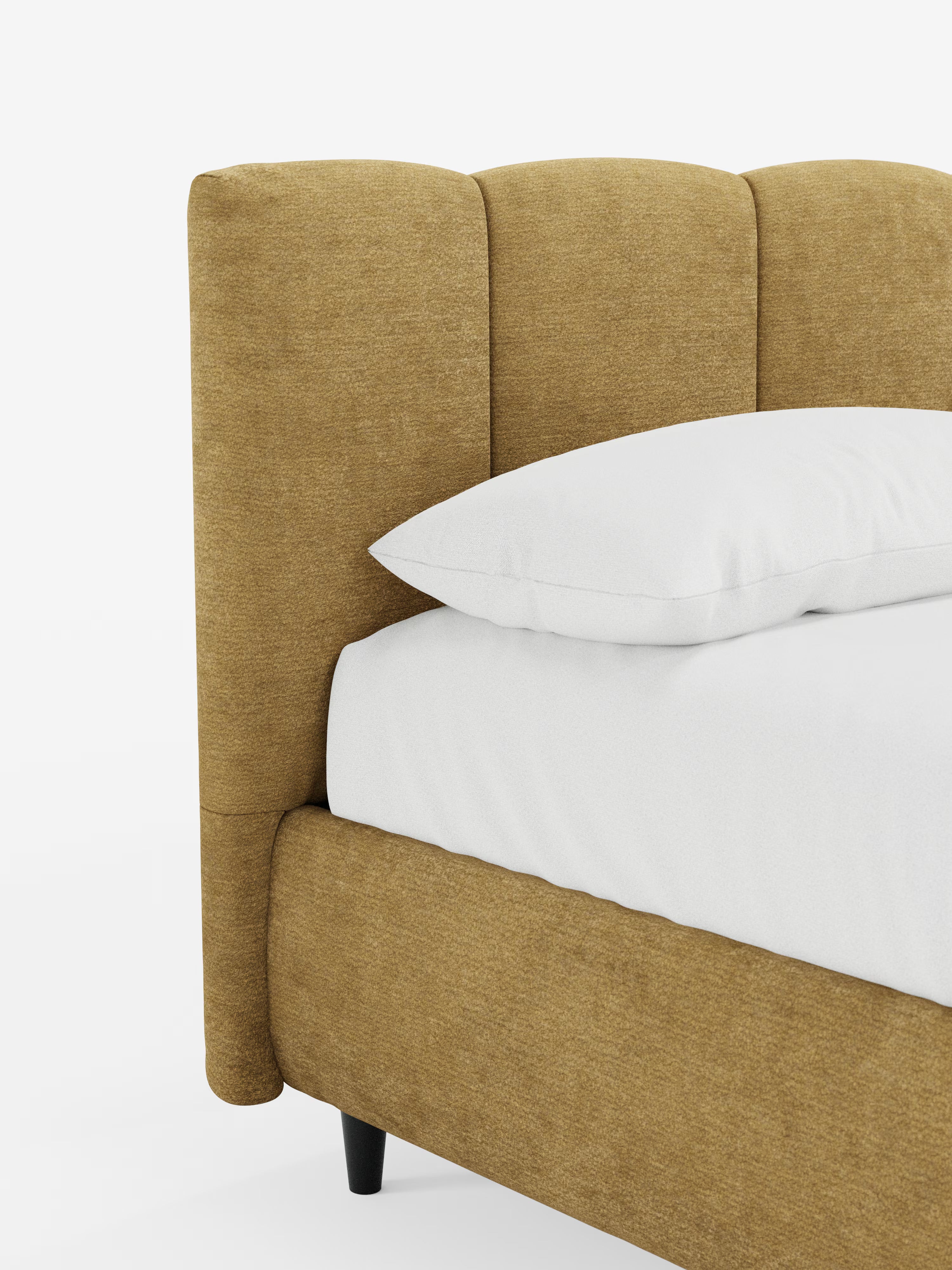 Un primo piano del letto imbottito ARKAM con contenitore e testiera a lavorazione verticale di Letti.store mette in risalto il suo tessuto giallo senape, certificato Oeko-Tex®, e il suo design shabby chic. Il letto presenta una testiera imbottita con cuciture verticali, impreziosita da cuscini e biancheria da letto bianchi. Poggia su corte gambe nere su uno sfondo bianco a tinta unita, che ne sottolinea lo stile moderno e la finitura materica.