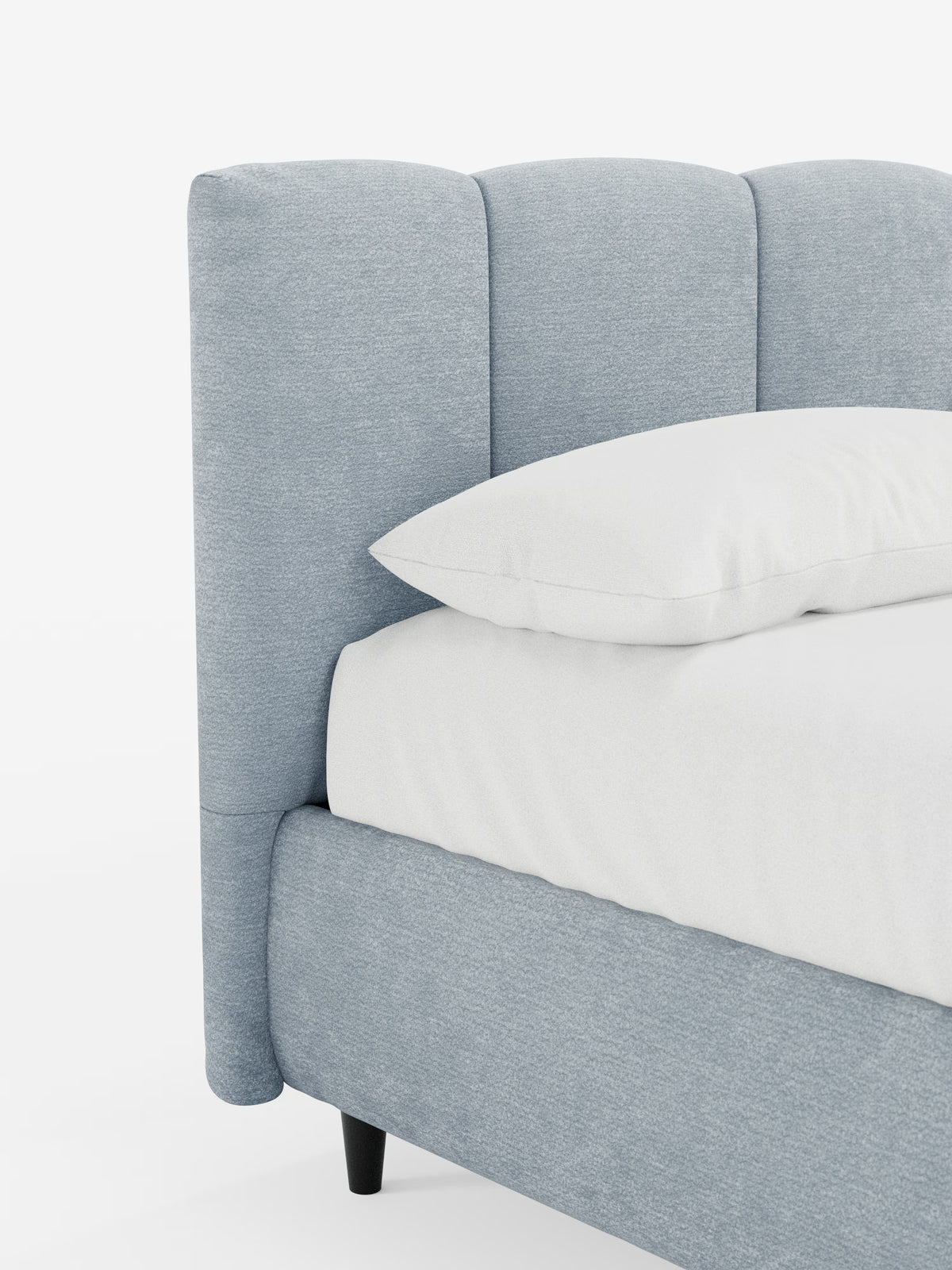 Un primo piano del letto imbottito ARKAM con contenitore e testiera a lavorazione verticale di Letti.store, caratterizzato da una testiera e da una struttura rivestite in tessuto azzurro certificato Oeko-Tex® con dettagli a pannelli verticali. Il letto è abbinato a un materasso e a un cuscino bianchi e poggia su eleganti gambe affusolate nere su uno sfondo bianco a tinta unita.