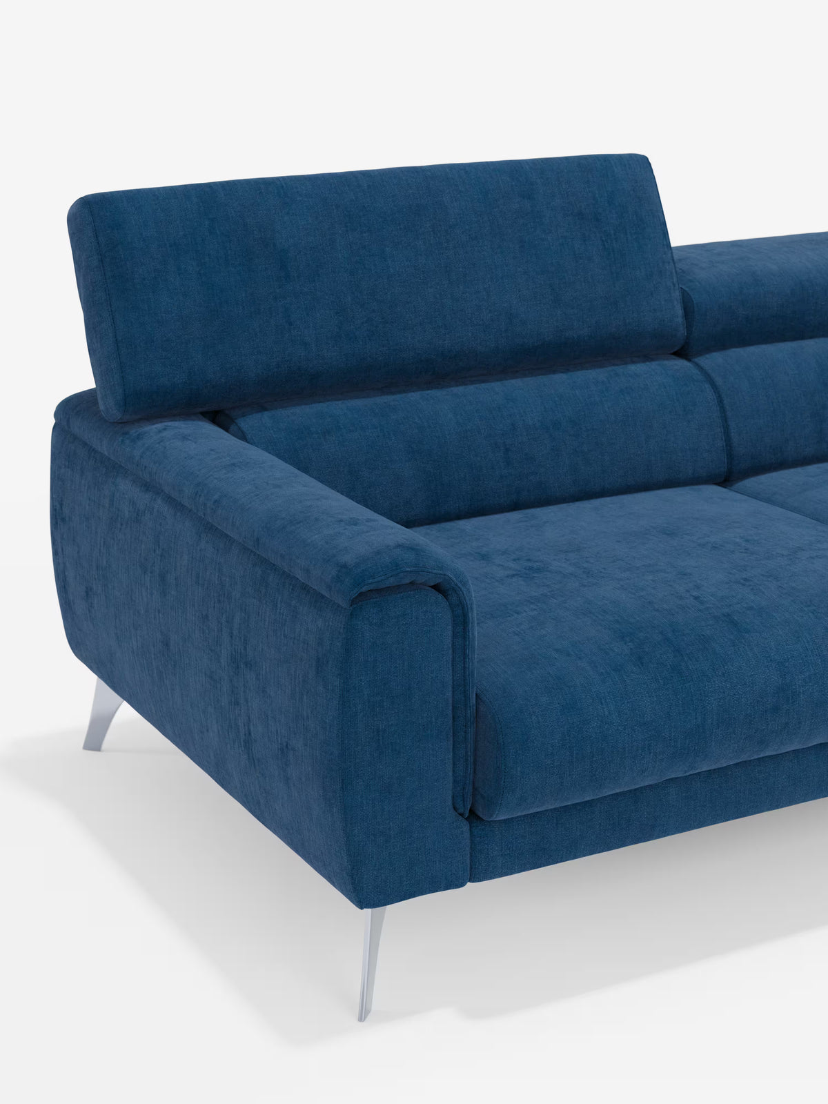 Il divano Caravaggio a 2 e 3 posti di Divani.Store, rivestito in elegante tessuto T31 resistente alle macchie, è un divano componibile contemporaneo in velluto blu, ideale per un soggiorno in stile contemporaneo. È dotato di sedute estensibili e poggiatesta reclinabili, con eleganti gambe angolate in metallo argentato e ampi braccioli. Il lussuoso rivestimento risalta sullo sfondo bianco a tinta unita, con solo una parte del divano visibile.