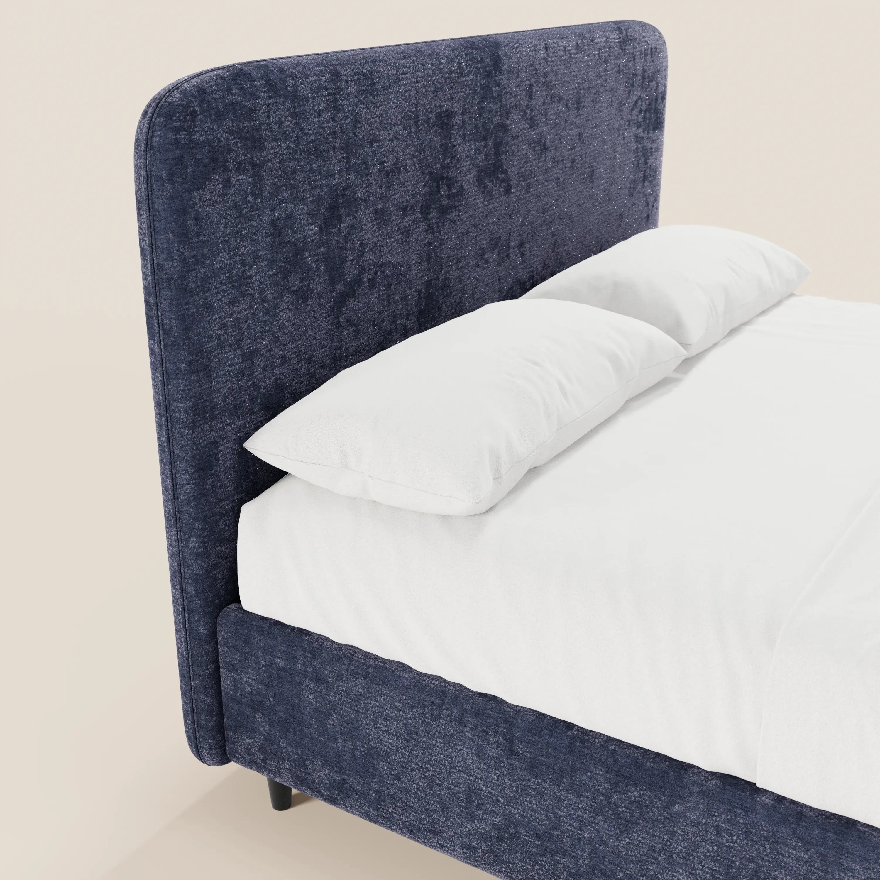 Un primo piano del letto imbottito KAELOS minimal di Letti.store mette in risalto la sua testiera alta e arrotondata in ciniglia blu, i cuscini bianchi e il lenzuolo bianco. Le gambe alte e lo spazio contenitivo ne sottolineano il design moderno su uno sfondo chiaro e sobrio.