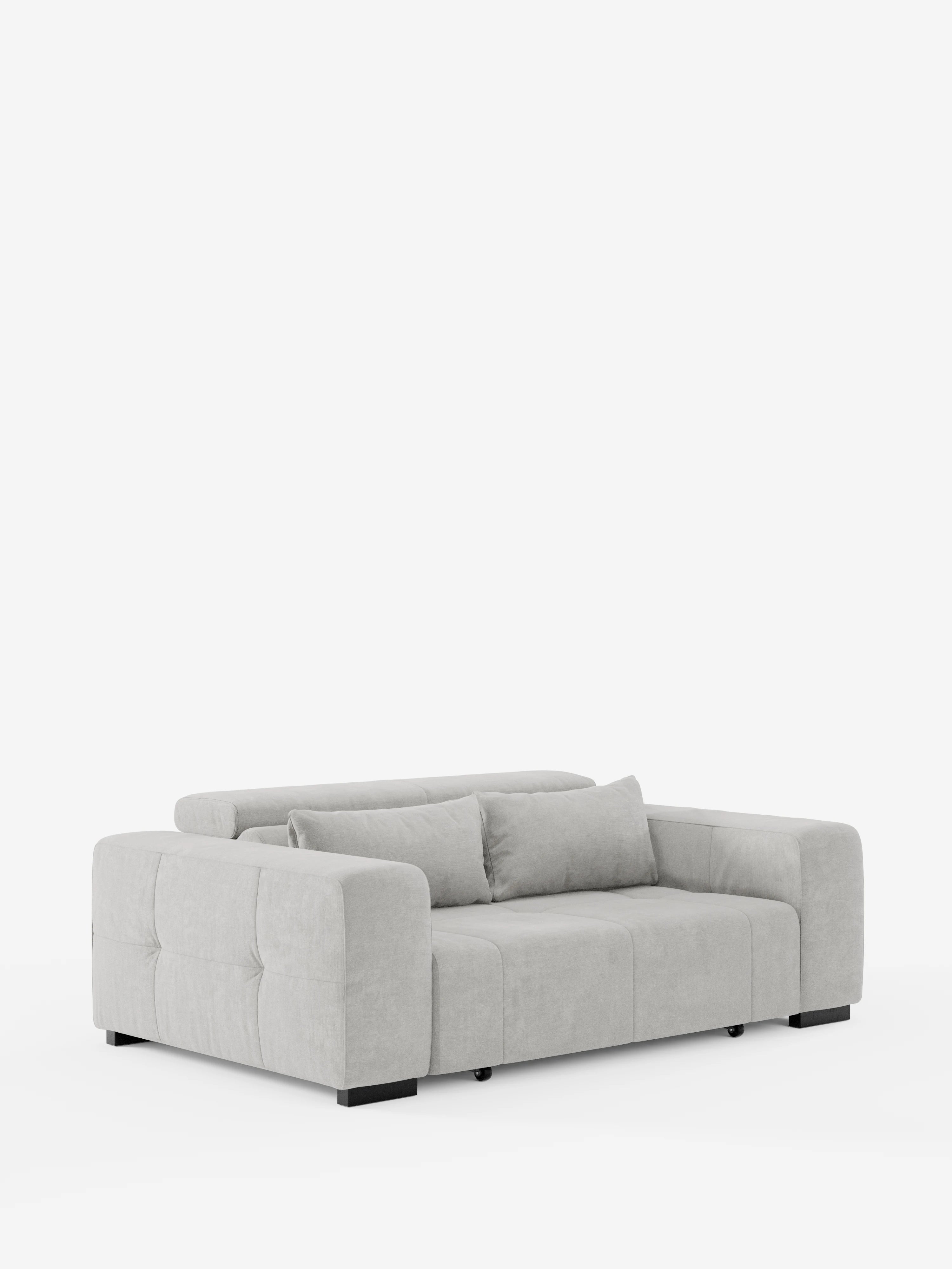 Un moderno divano Monarch con funzione relax elettrica per l’allungamento delle sedute e poggiatesta reclinabile di Divani.Store, rivestito in tessuto T31 grigio chiaro, morbido e resistente alle macchie, presenta sedute avvolgenti, ampi braccioli, due cuscini coordinati e fianchi trapuntati che ricordano un divano capitonné. Il divano poggia su gambe a blocco nere su uno sfondo bianco.