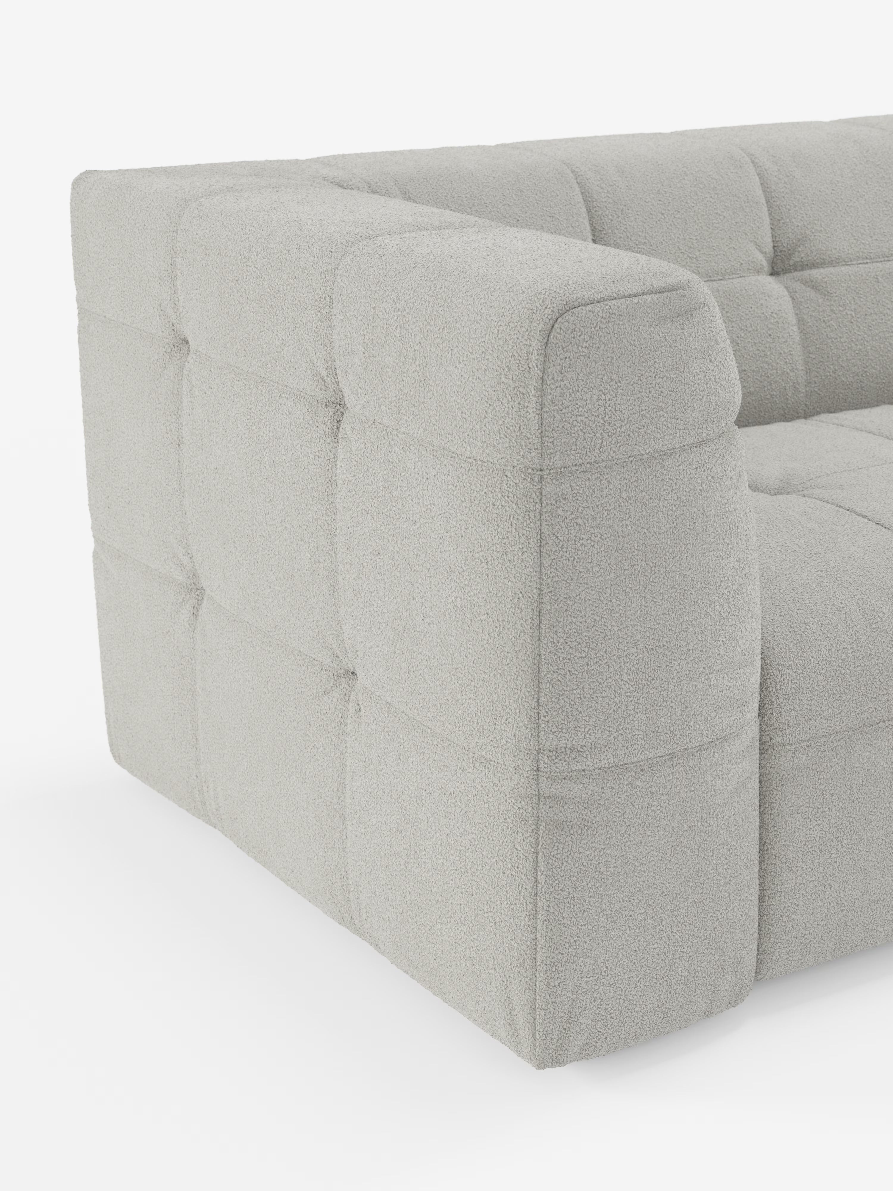 Un primo piano del divano angolare componibile e modulare Mosaic in bouclé: capitonné e design in tessuto smacchiabile T21 di Divani.Store, caratterizzato da una moderna struttura modulare grigio chiaro con morbido rivestimento in bouclé dalla trama rigata. I braccioli e la seduta presentano un'imbottitura squadrata e profonda con dettagli trapuntati, che conferiscono un aspetto lussuoso e contemporaneo sullo sfondo bianco.