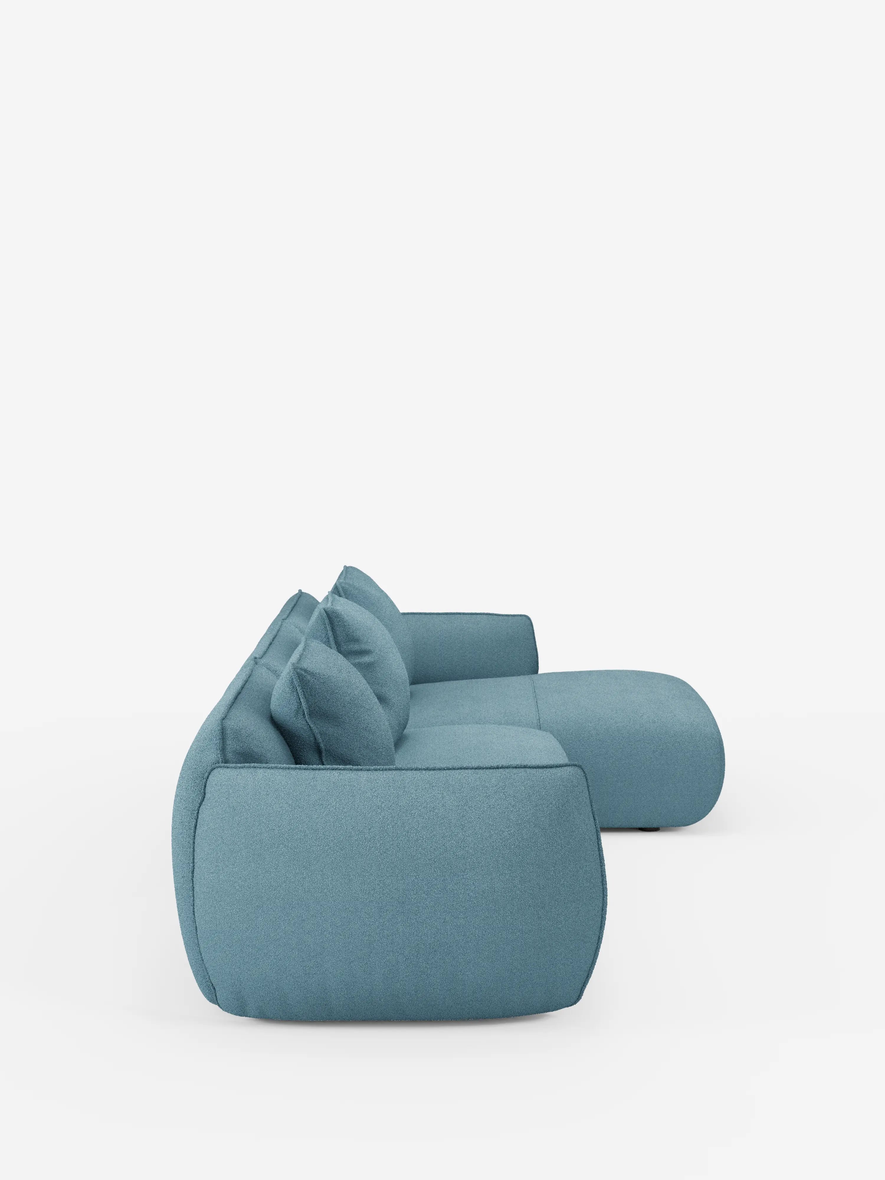 Vista laterale del divano angolare con penisola componibile Nimbus di Divani.Store, rivestito in tessuto T33 azzurro chiaro, morbido, effetto cotone e resistente alle macchie. Il divano presenta un design minimalista con cuscini soffici e bordi arrotondati, che risaltano su uno sfondo bianco a tinta unita. Sono visibili due cuscini dello schienale, che ne sottolineano lo stile accogliente e contemporaneo.