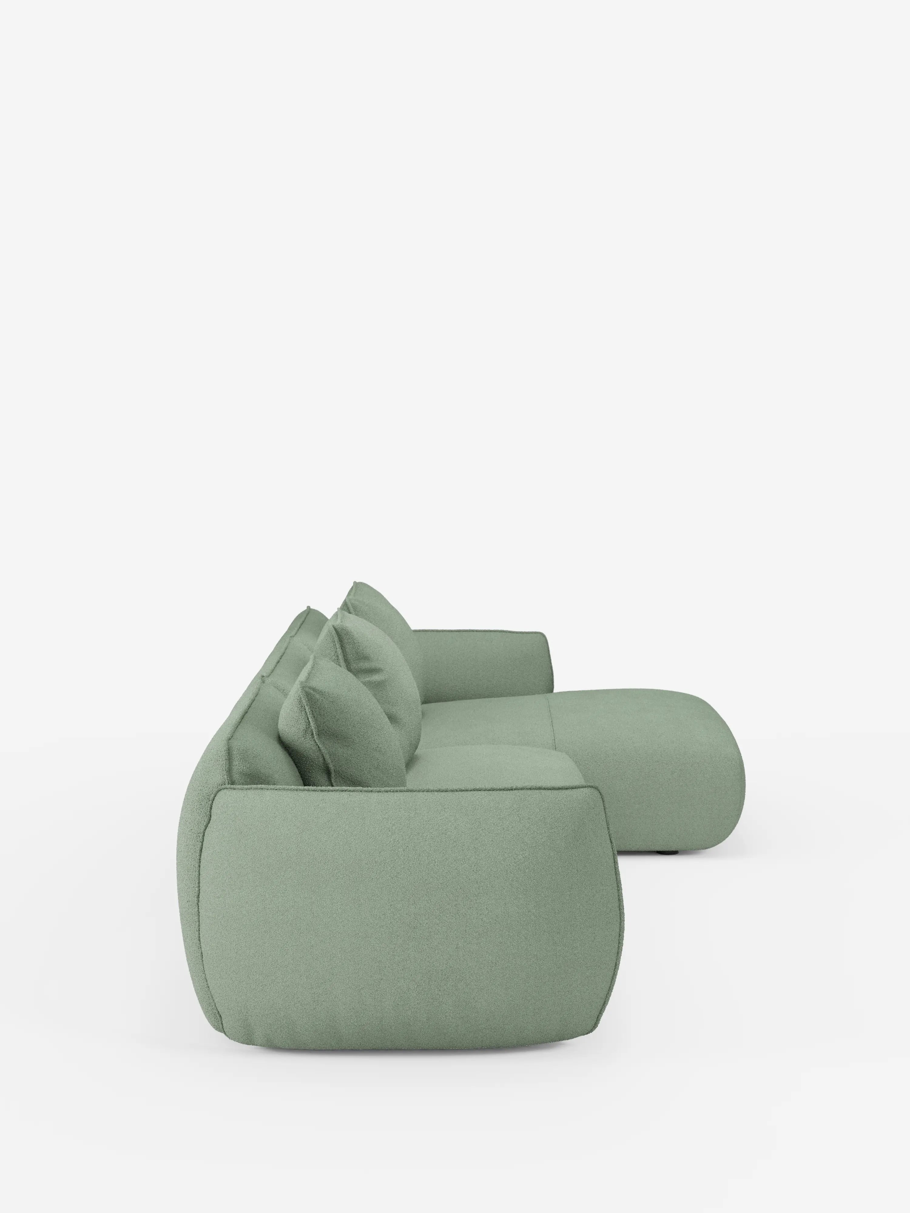 Un moderno divano angolare con penisola componibile Nimbus di colore verde chiaro, firmato Divani.Store, rivestito in morbido tessuto effetto cotone antimacchia (T33), è raffigurato di profilo su uno sfondo bianco a tinta unita. Questo divano presenta bordi arrotondati, tre cuscini coordinati, una seduta bassa e profonda e un design minimalista e contemporaneo.