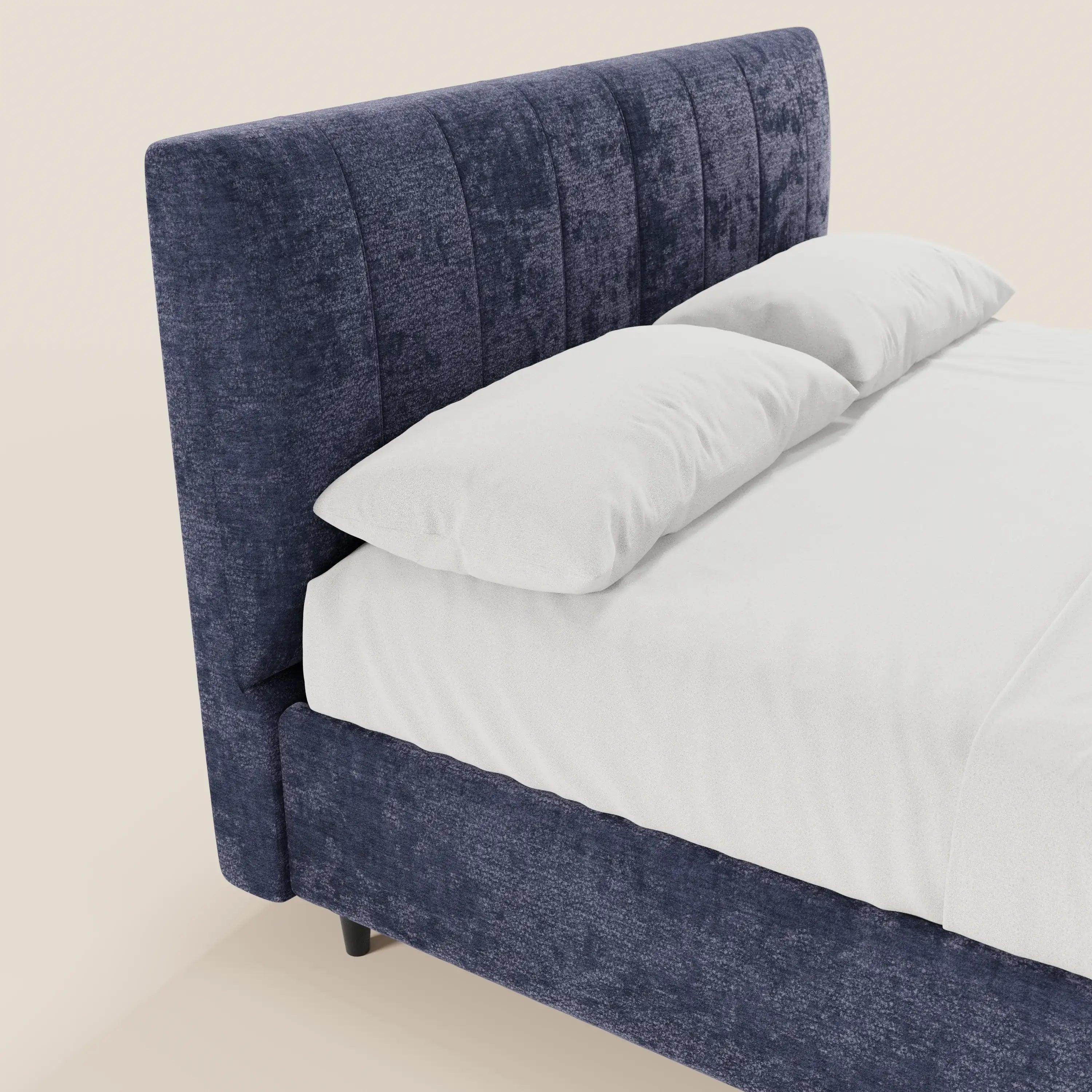 Un primo piano del letto imbottito con contenitore ONYX di Letti.store, caratterizzato da un’alta testiera verticale in tessuto Oeko-Tex® blu scuro, lenzuola bianche lisce e due grandi cuscini bianchi su uno sfondo beige neutro.