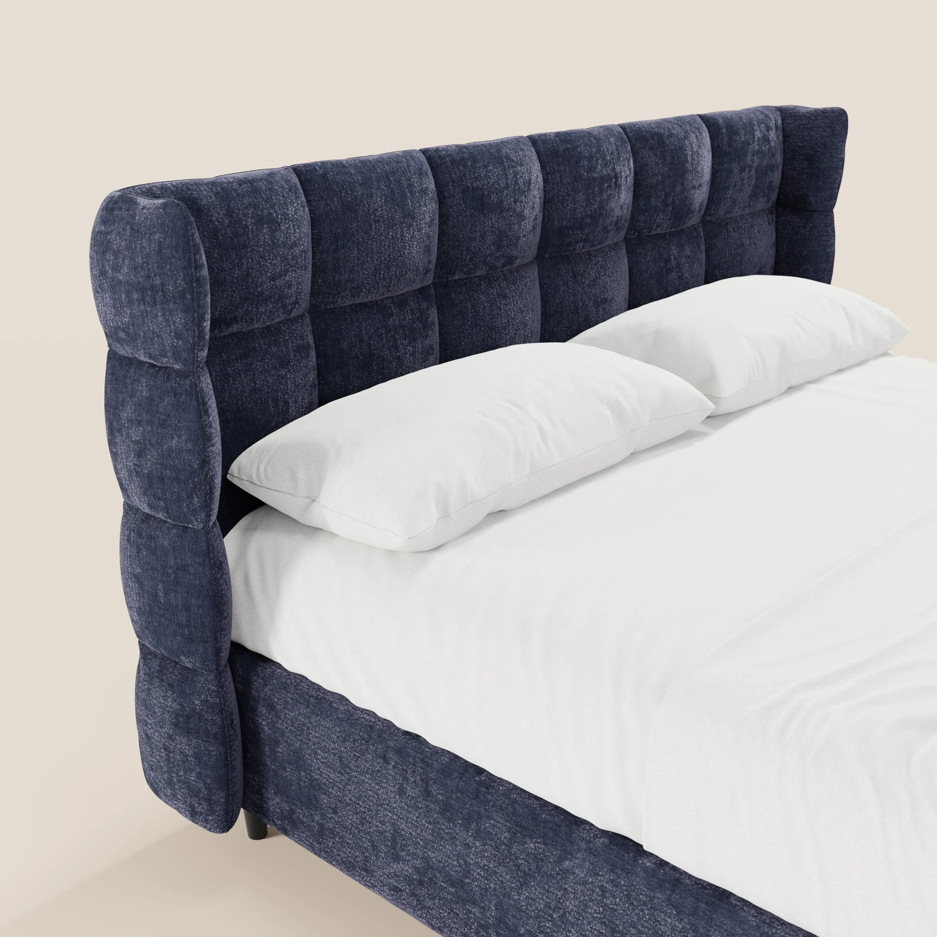Il letto imbottito RAGNAR di Letti.store è caratterizzato da un tessuto blu scuro certificato Oeko-Tex®, da un'alta testiera avvolgente capitonné e da biancheria da letto bianca con due cuscini, il tutto disposto in diagonale su uno sfondo neutro.