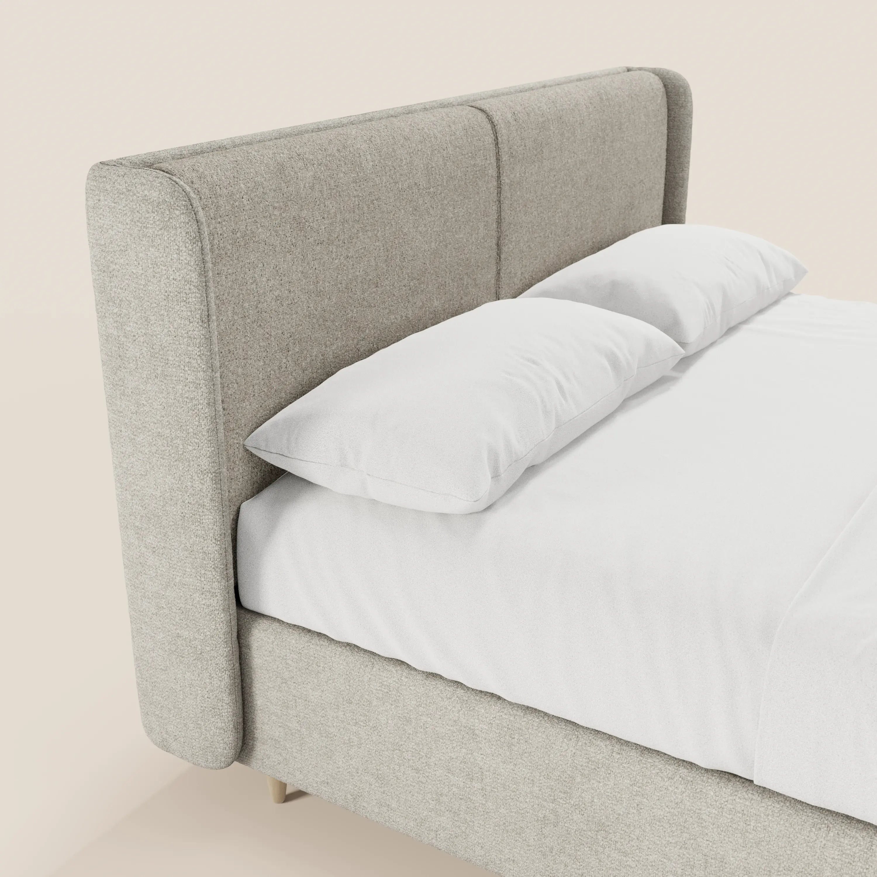 Un primo piano del letto imbottito bicolore VALKIRIA di Letti.store, con una testiera curva avvolgente e cuscini schienali. Il letto presenta un rivestimento grigio chiaro, biancheria da letto bianca e due cuscini, in stile minimal contemporaneo italiano.