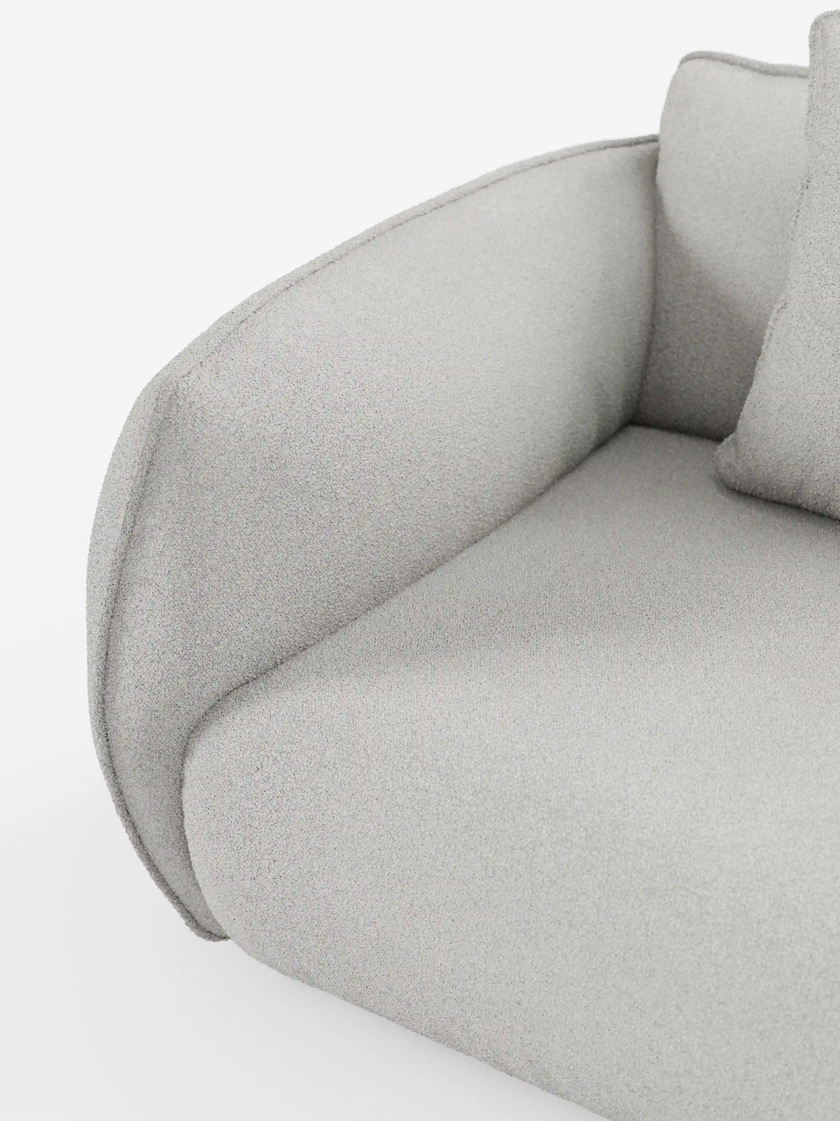 Primo piano del bracciolo e della seduta del divano modulare a 3 posti Nimbus di Divani.Store. Il tessuto T33 grigio chiaro, smacchiabile ed effetto cotone, appare ruvido al tatto e morbido, con bordi puliti e arrotondati e un design minimalista. È visibile una parte del cuscino dello schienale. Lo sfondo bianco a tinta unita mette in risalto le linee morbide del divano.