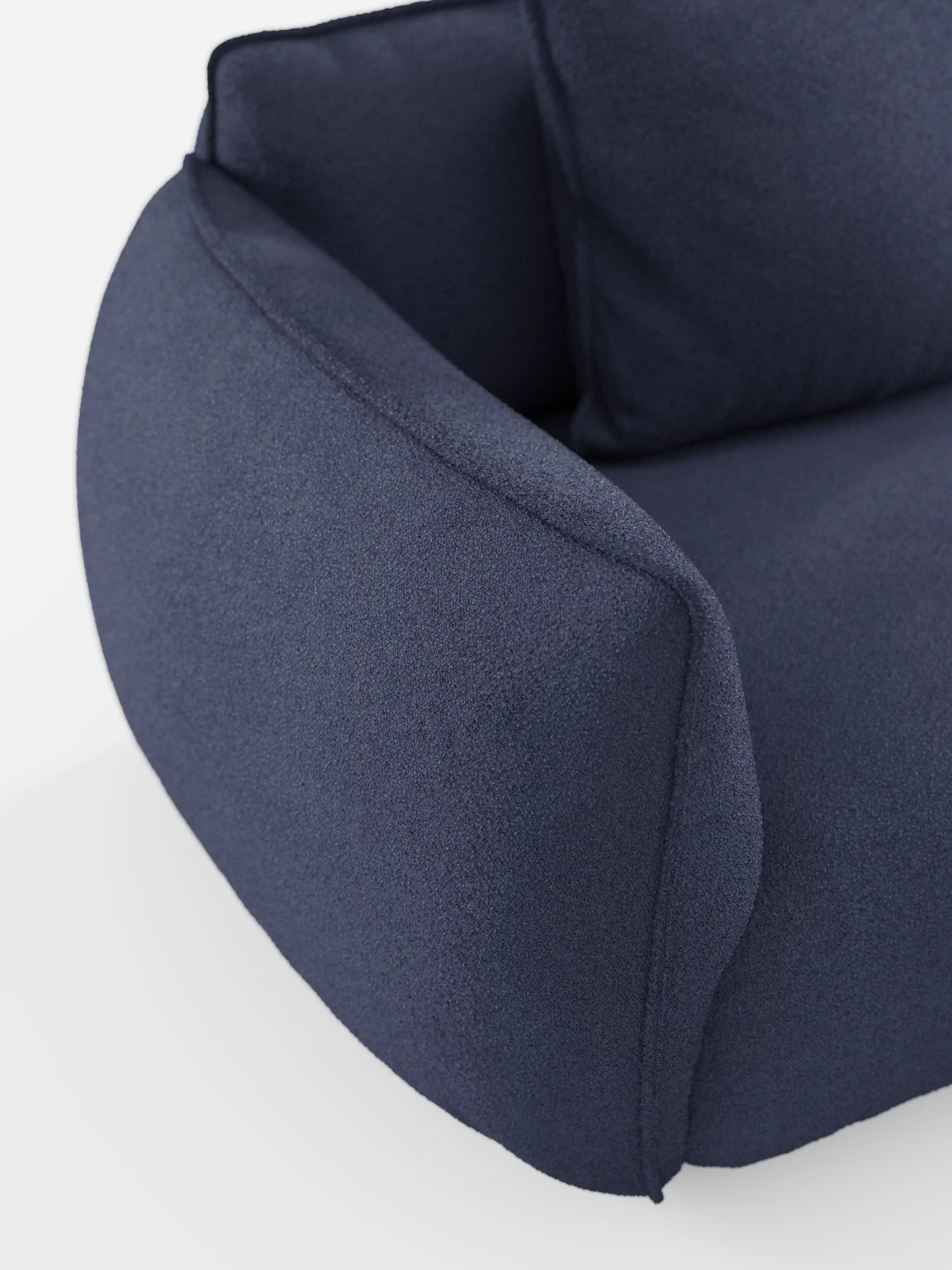Primo piano del divano angolare con penisola Nimbus di Divani.Store, caratterizzato da braccioli e schienale morbidi e arrotondati. Questo moderno divano modulare è rivestito in tessuto T33 blu scuro effetto cotone, lavabile e dalla trama ruvida, con cuscini spessi e un design minimalista. Lo sfondo bianco mette in risalto le forme eleganti del divano e i dettagli del tessuto.