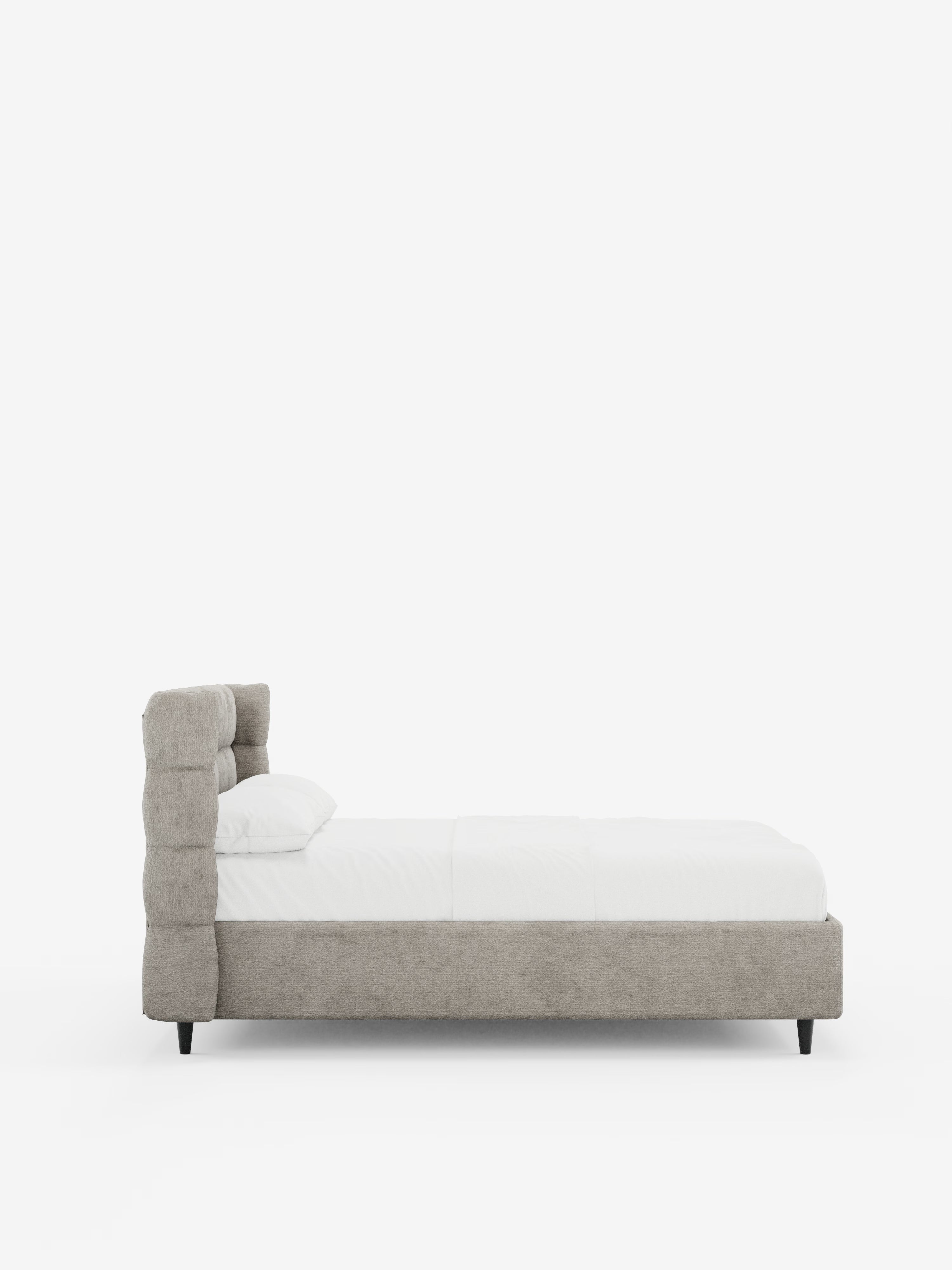 Vista laterale del letto imbottito RAGNAR con contenitore e testiera capitonné avvolgente di Letti.store, caratterizzato da un’elegante testiera e da una struttura in tessuto grigio chiaro certificato Oeko-Tex® con dettagli capitonné, gambe corte nere e biancheria da letto bianca curata nei dettagli con un cuscino, il tutto su uno sfondo bianco a tinta unita.