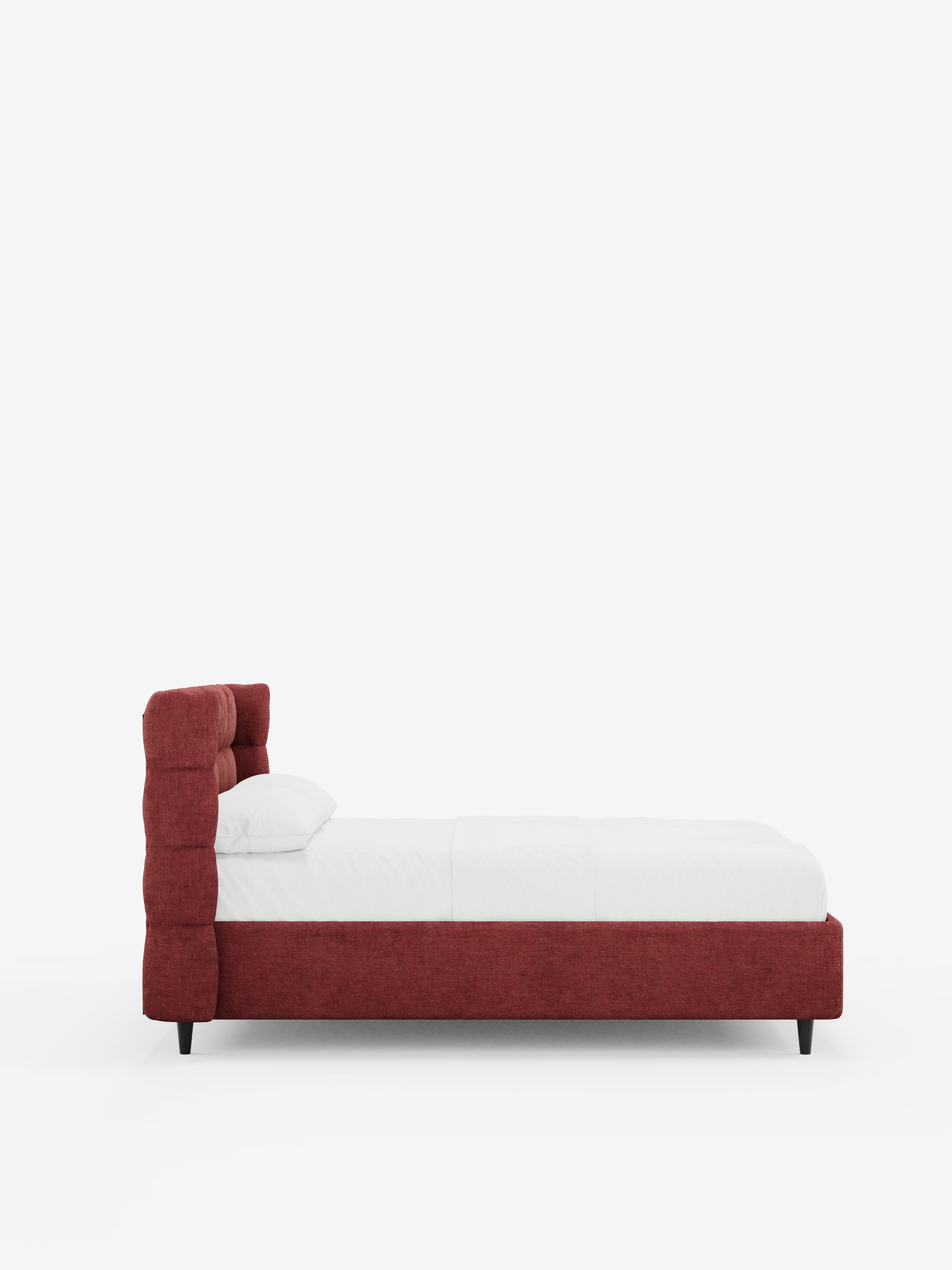 Una vista laterale del letto imbottito RAGNAR con contenitore e testiera capitonné avvolgente di Letti.store, caratterizzato da un’alta testiera imbottita rossa trapuntata nel classico stile capitonné, da un’elegante biancheria da letto bianca con un unico cuscino e da gambe nere, il tutto su uno sfondo bianco a tinta unita.