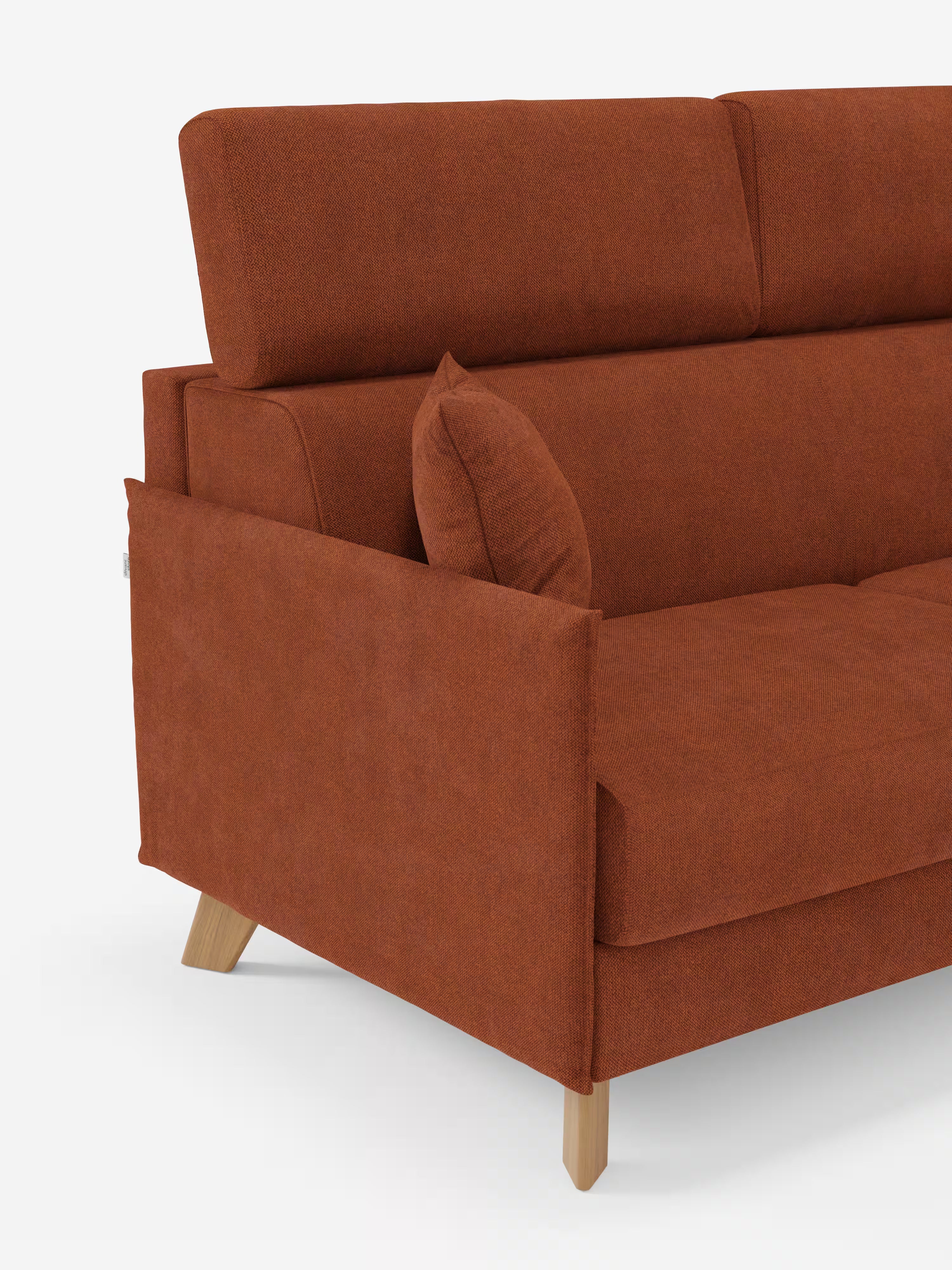 Un moderno divano letto matrimoniale Sole color ruggine di Divani.Store, caratterizzato da un design scandinavo compatto con gambe angolari in legno, braccioli imbottiti e un cuscino coordinato. Questo divano è dotato di poggiatesta reclinabili e di un morbido rivestimento realizzato in tessuto T23, 100% sfoderabile e resistente alle macchie. Immagine scattata su uno sfondo bianco a tinta unita, con solo il lato sinistro visibile.