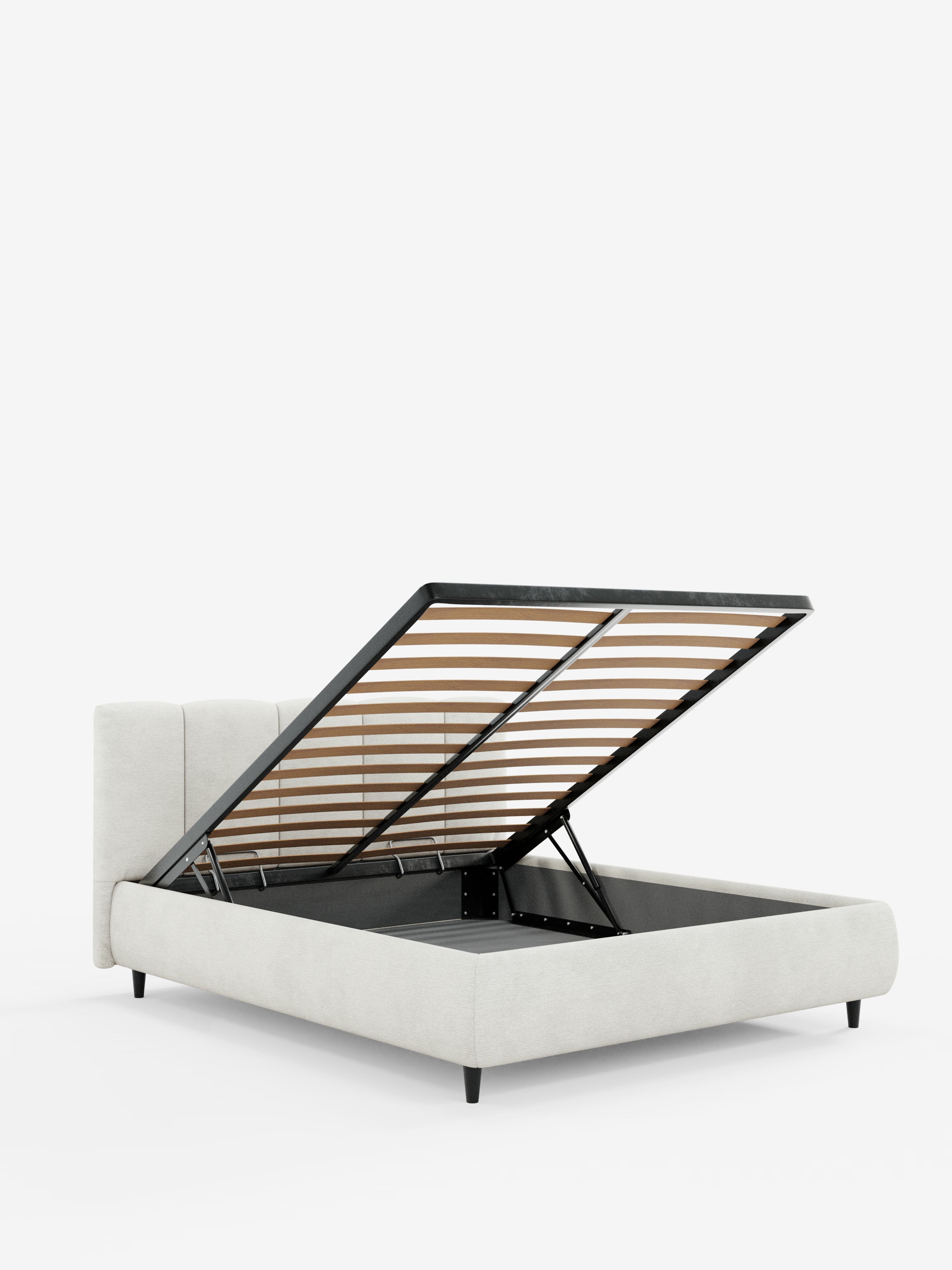 Il letto imbottito ARKAM di Letti.store presenta una testiera con cuciture verticali e una struttura in tessuto chiaro certificato Oeko-Tex®, in stile shabby chic. Sostenuto da gambe nere, questo letto moderno è dotato di una base a doghe rialzata che, una volta sollevata, rivela un ampio vano contenitore. Su uno sfondo bianco a tinta unita, l’immagine mette in risalto le linee pulite e l’eleganza funzionale del letto.