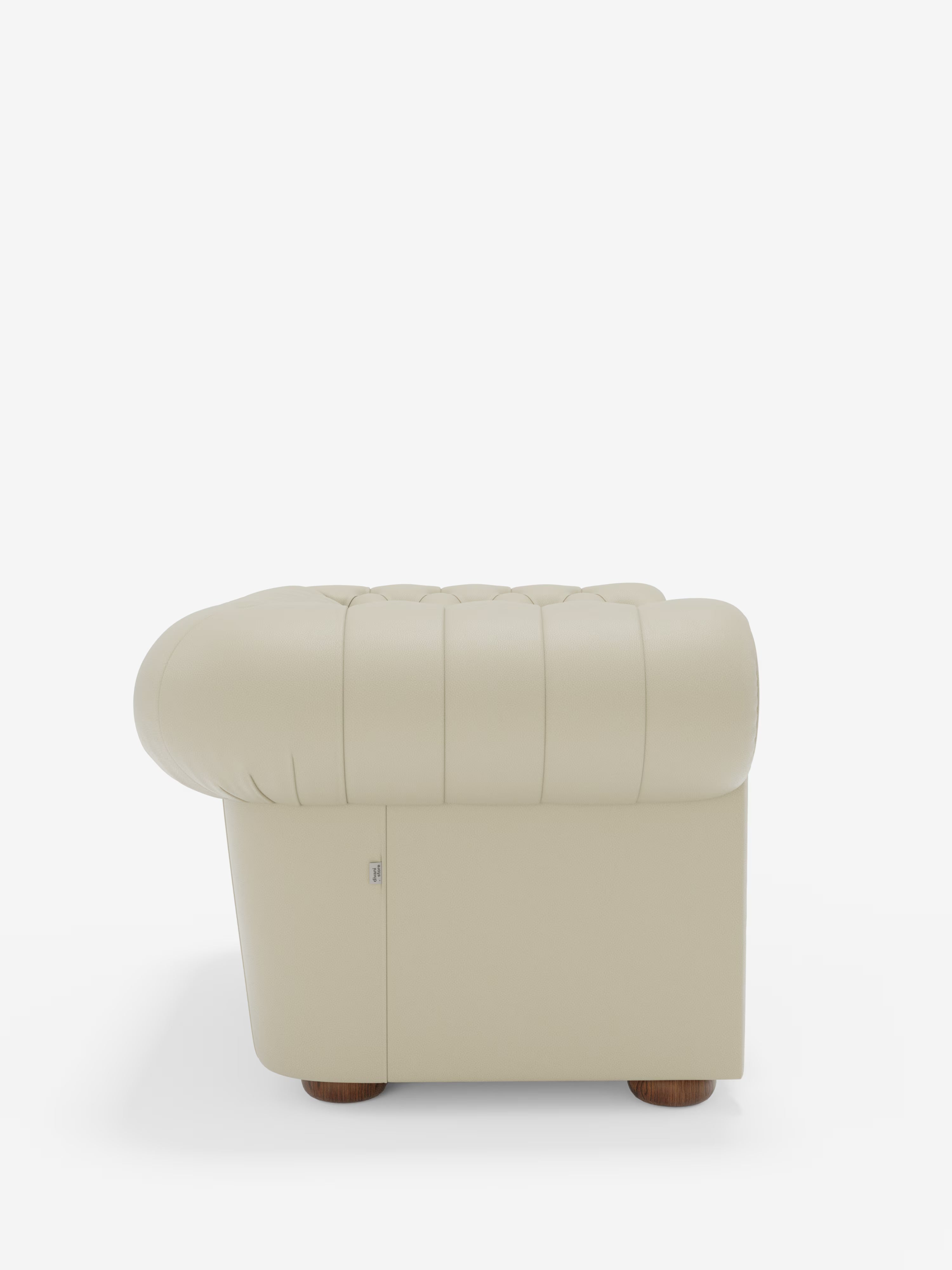 Vista laterale della poltrona Chester in vera pelle spessorata con capitonné artigianale di Divani.Store, rivestita in pelle beige con capitonné artigianale. Caratterizzata da morbidi braccioli e schienale arrotondati, questa poltrona poggia su piedini corti e rotondi in legno. In primo piano su uno sfondo bianco a tinta unita che mette in risalto le eleganti curve della poltrona e la morbida trama della pelle.