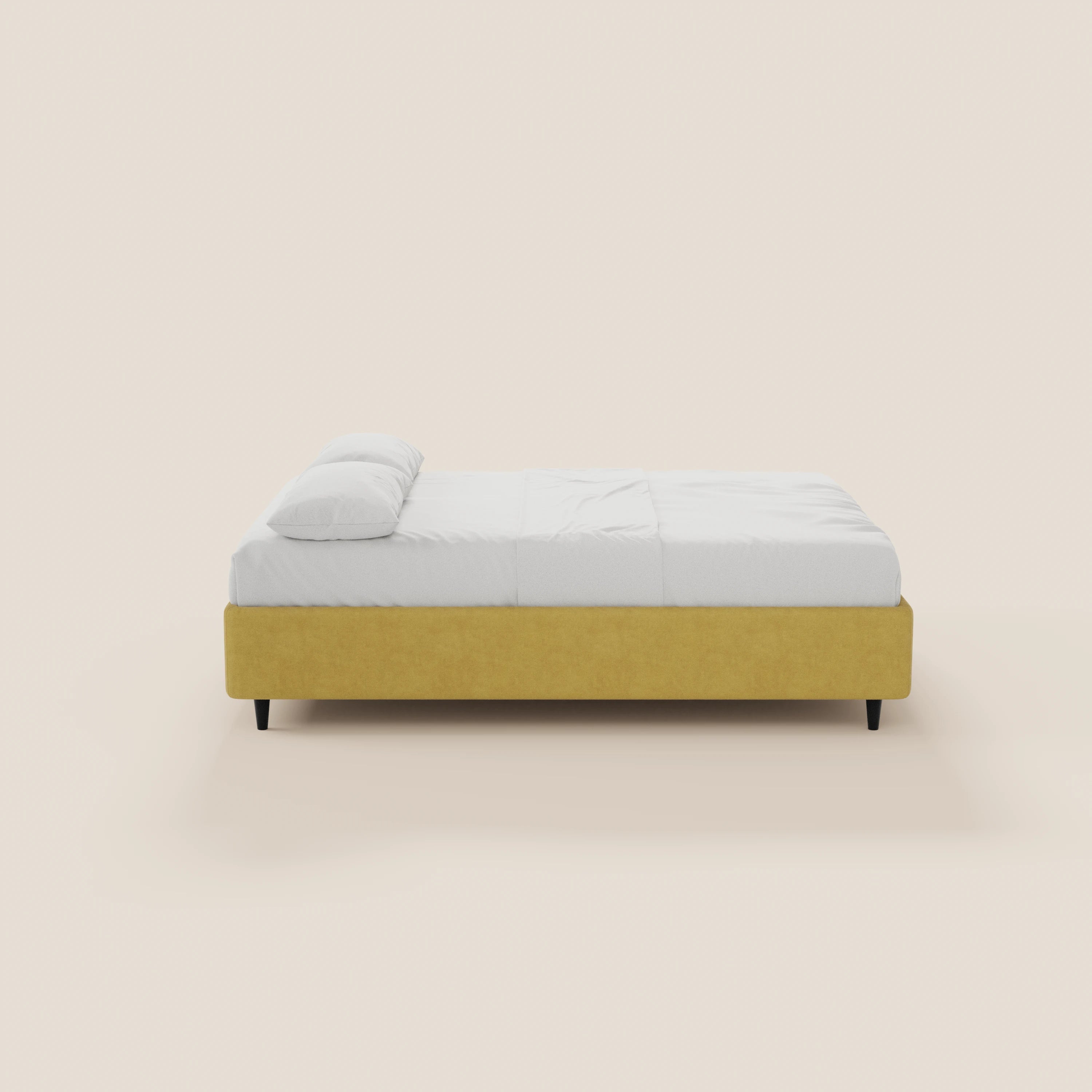 Il letto sommier imbottito ERON di Letti.store presenta una base in tessuto impermeabile giallo senape certificato Oeko-Tex, gambe nere, biancheria da letto bianca e due cuscini bianchi. Ripreso di profilo su uno sfondo beige chiaro a tinta unita, il suo design è semplice e minimalista.