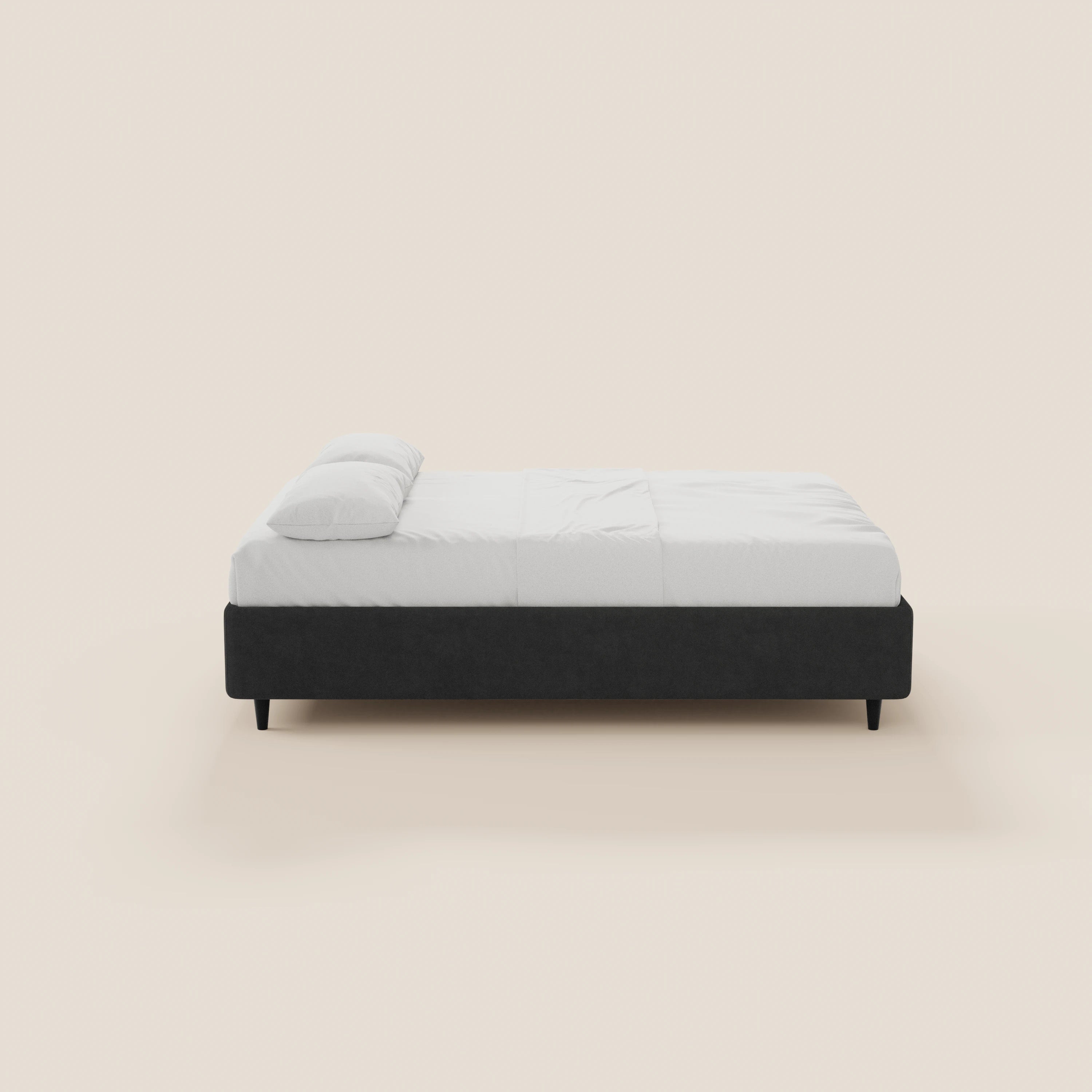 Il letto sommier imbottito ERON di Letti.store presenta una struttura in tessuto nero impermeabile certificato Oeko-Tex, materasso e lenzuola bianchi, gambe corte e linee essenziali. Nell’immagine è raffigurato di profilo su uno sfondo beige chiaro, in stile moderno e minimalista, con vano contenitore.