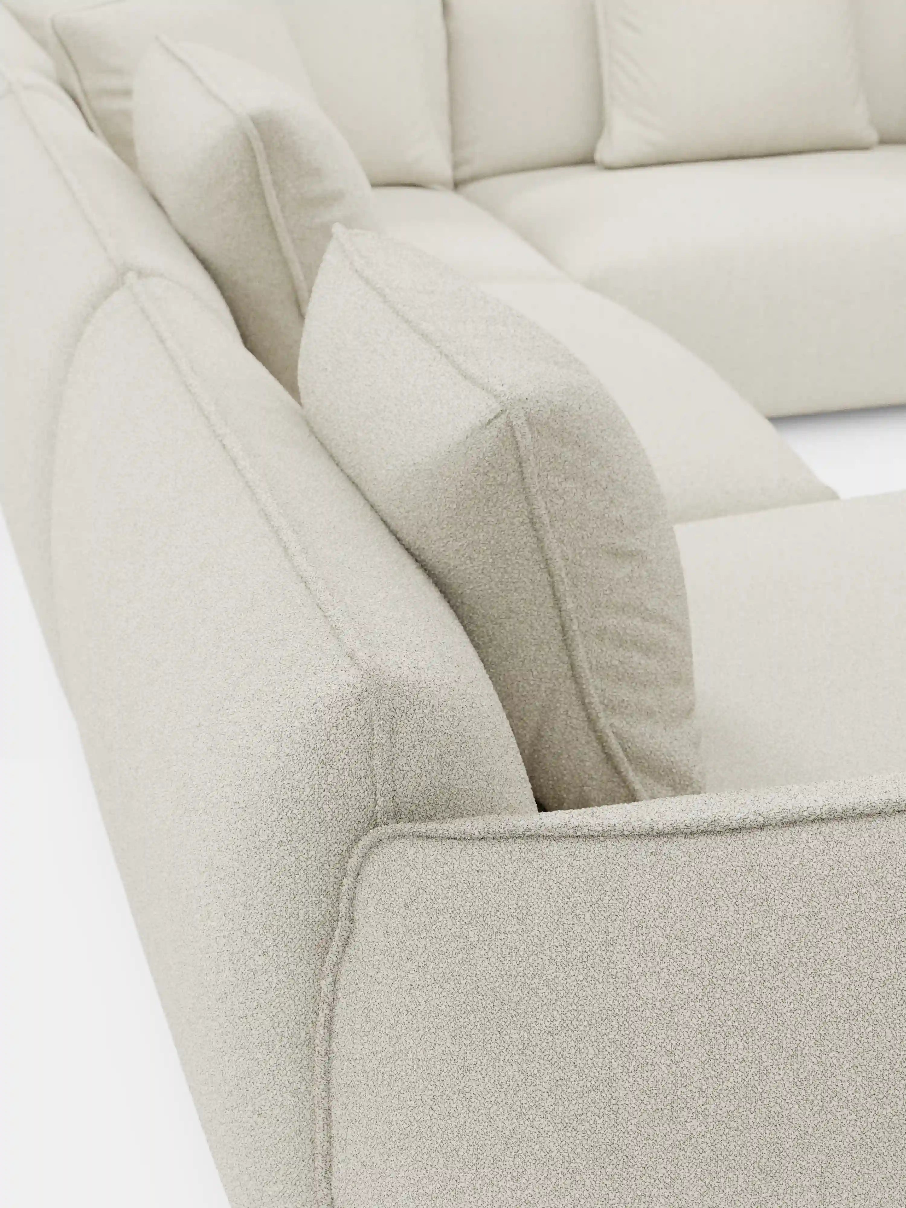 Primo piano del divano angolare panoramico componibile Nimbus con penisola e angolo in tessuto smacchiabile T33 di Divani.Store, un moderno divano componibile italiano color beige caratterizzato da linee pulite, cuscini rettangolari rigidi e rivestimento in tessuto testurizzato antimacchia. Su uno sfondo bianco, l’angolo mette in risalto la vista posteriore e laterale, sottolineando sia la morbidezza che l’eleganza strutturata di questa sofisticata soluzione di seduta.