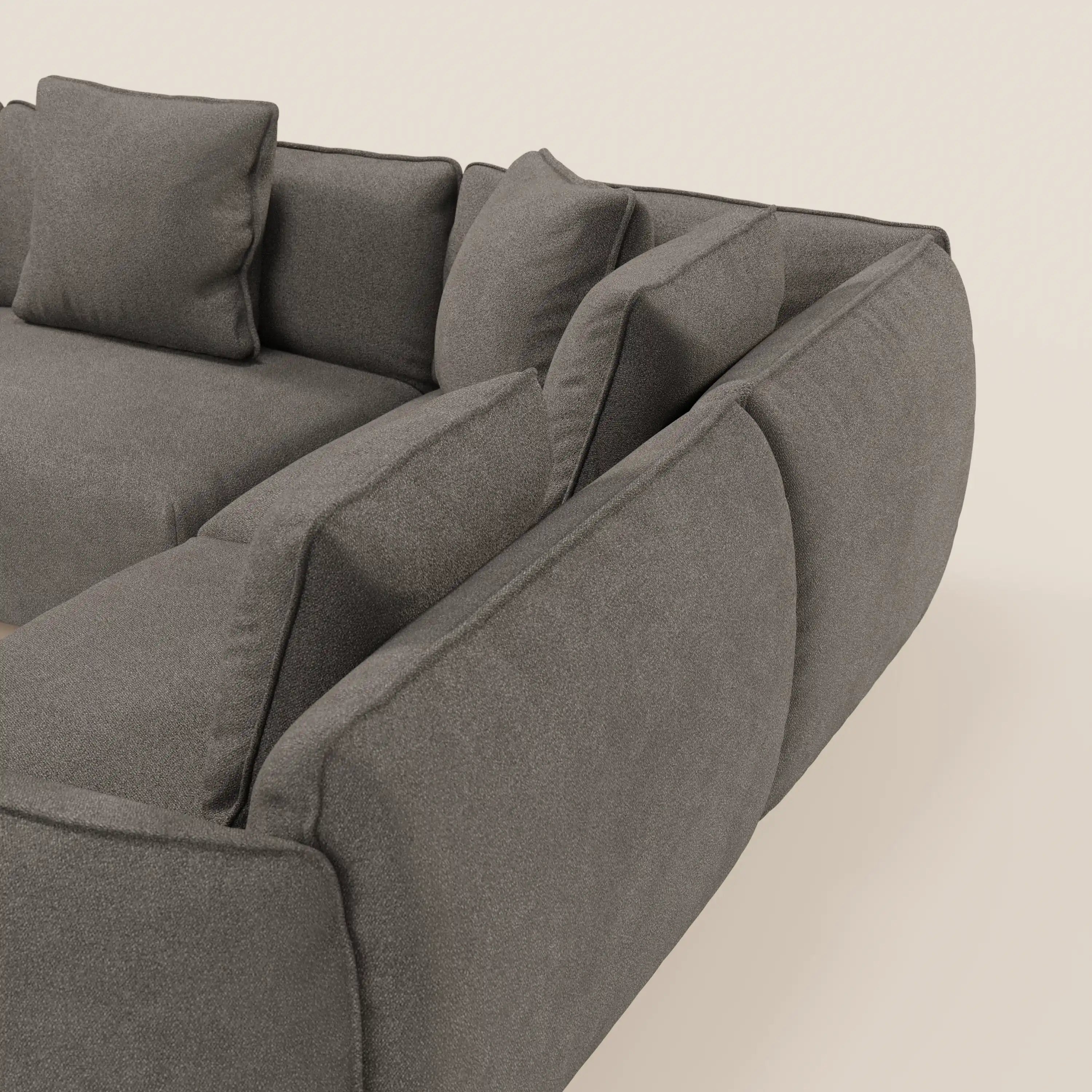 Una vista ravvicinata e angolata del divano angolare panoramico componibile Nimbus di Divani.Store, con il tessuto smacchiabile grigio t33, le linee pulite e i cuscini morbidi su uno sfondo beige chiaro. Prodotto in Italia.