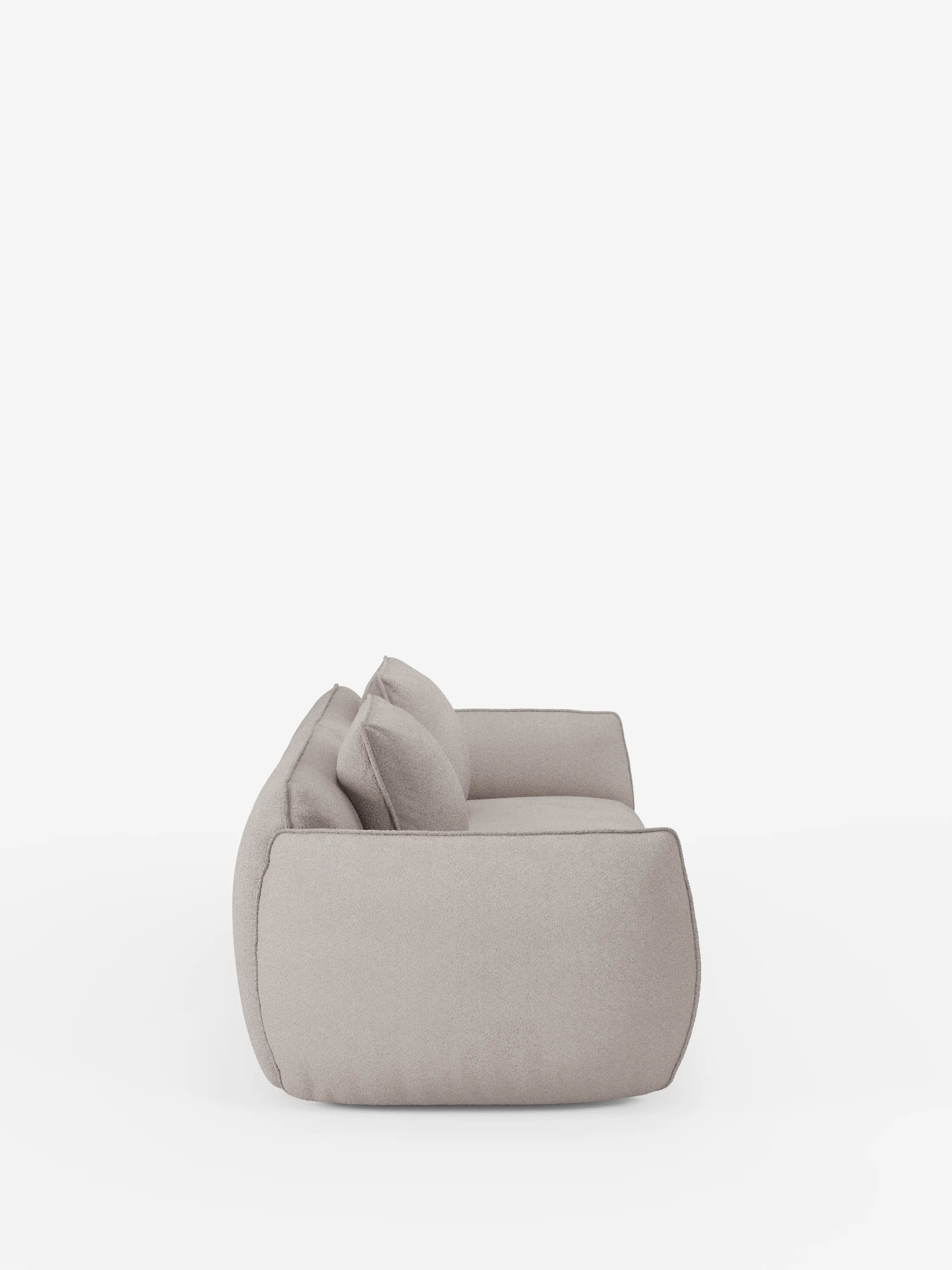 Vista laterale del divano Nimbus a 3 posti, modulare e componibile da 250 cm di Divani.Store, qui raffigurato in un tessuto moderno color beige chiaro con cuscini morbidi e bordi arrotondati. Il divano, rivestito in tessuto t33 effetto cotone, sfoderabile e resistente alle macchie, ha un'altezza ridotta da terra e un aspetto morbido e accogliente. È ripreso su uno sfondo bianco a tinta unita, senza altri oggetti visibili.