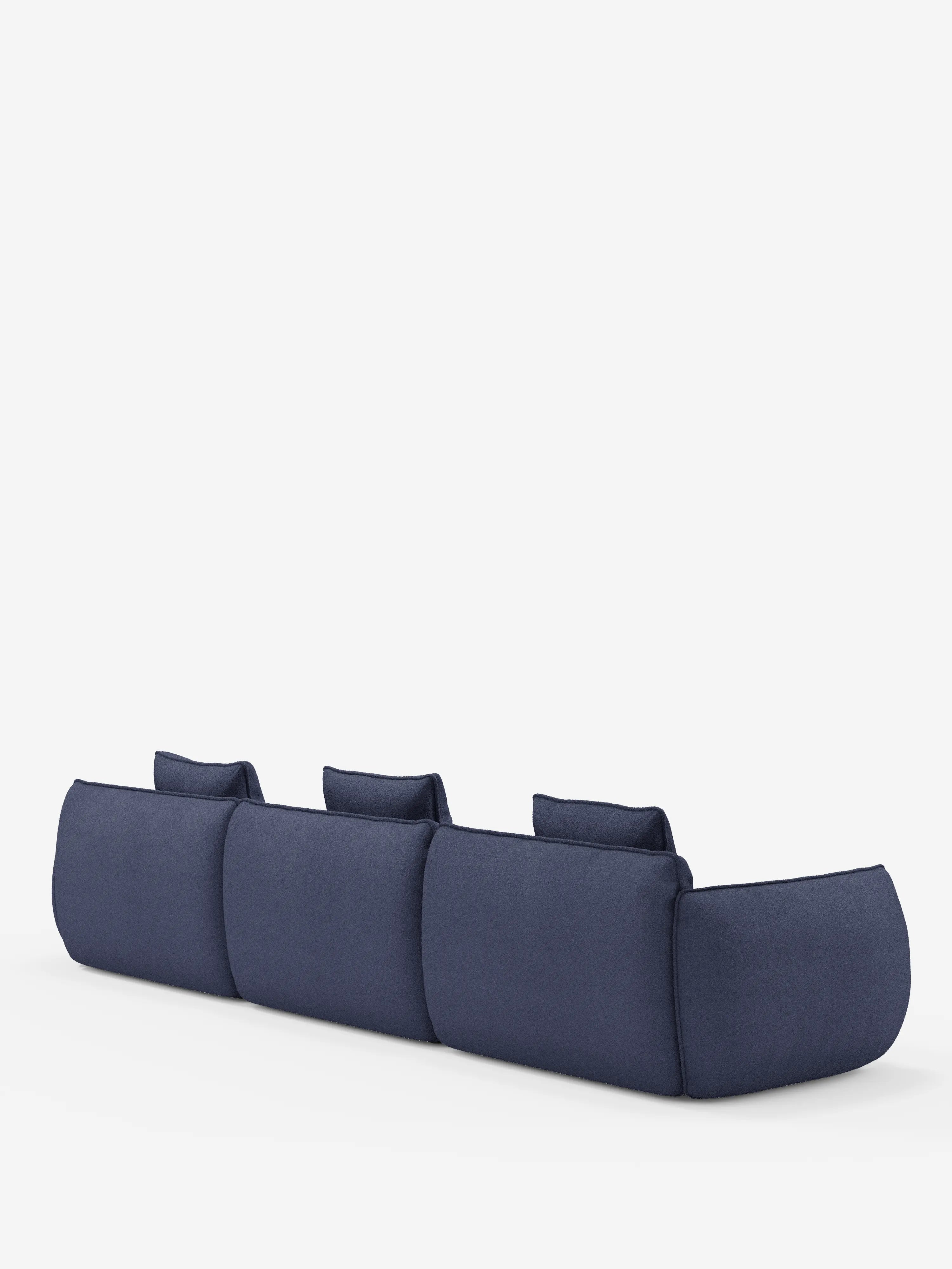 Un divano angolare con penisola componibile Nimbus a tre posti, di colore blu scuro, di Divani.Store, è raffigurato di spalle su uno sfondo bianco. Il divano componibile, rivestito in morbido tessuto effetto cotone antimacchia (T33), presenta cuscini soffici e arrotondati e tre poggiatesta bassi che conferiscono un look minimalista e contemporaneo, che ricorda un elegante divano modulare.