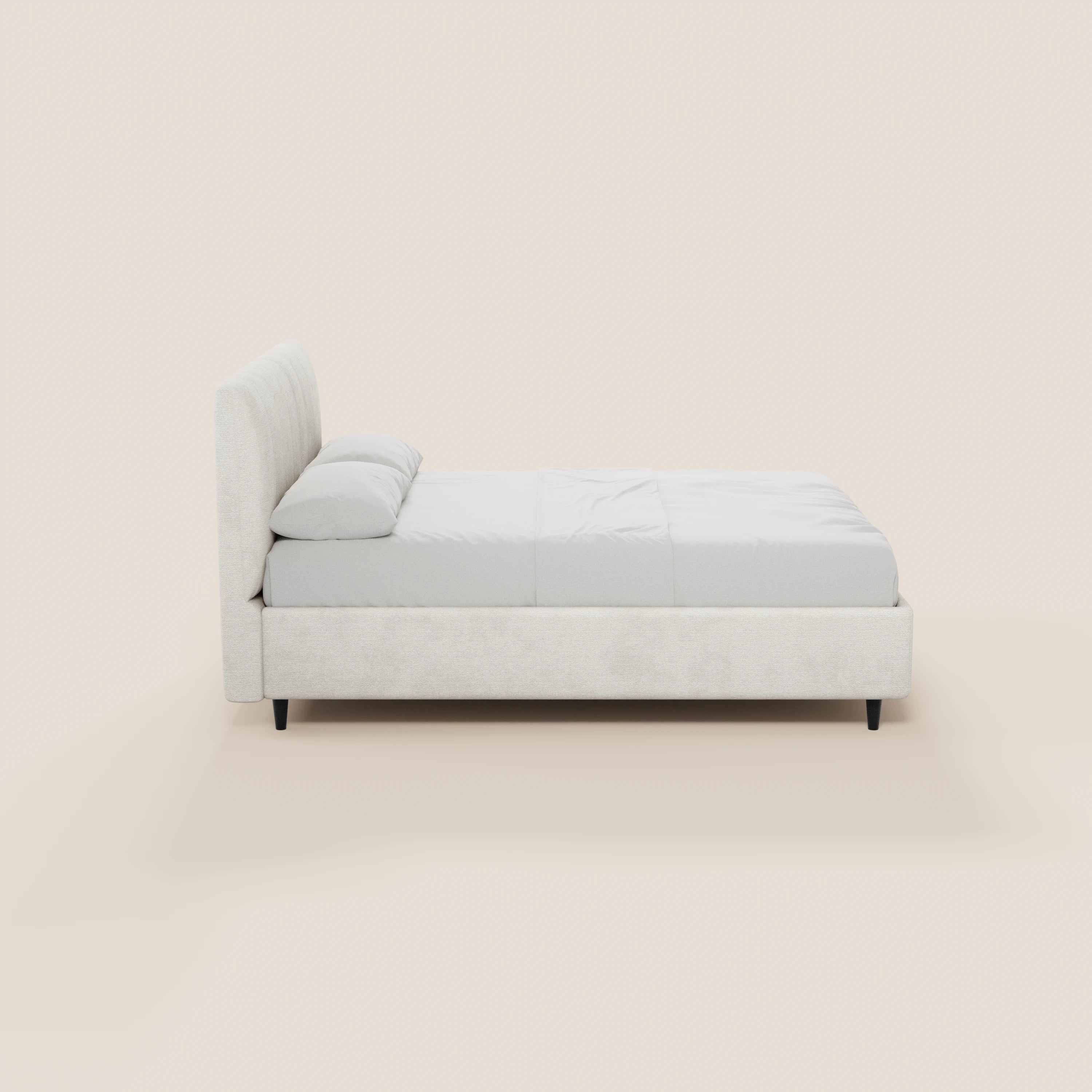 Il letto imbottito con contenitore ONYX di Letti.store presenta una testiera verticale in tessuto certificato Oeko-Tex®, una struttura imbottita, biancheria da letto bianca e due cuscini, il tutto su gambe corte nere; nella foto è raffigurato di profilo su uno sfondo beige chiaro.