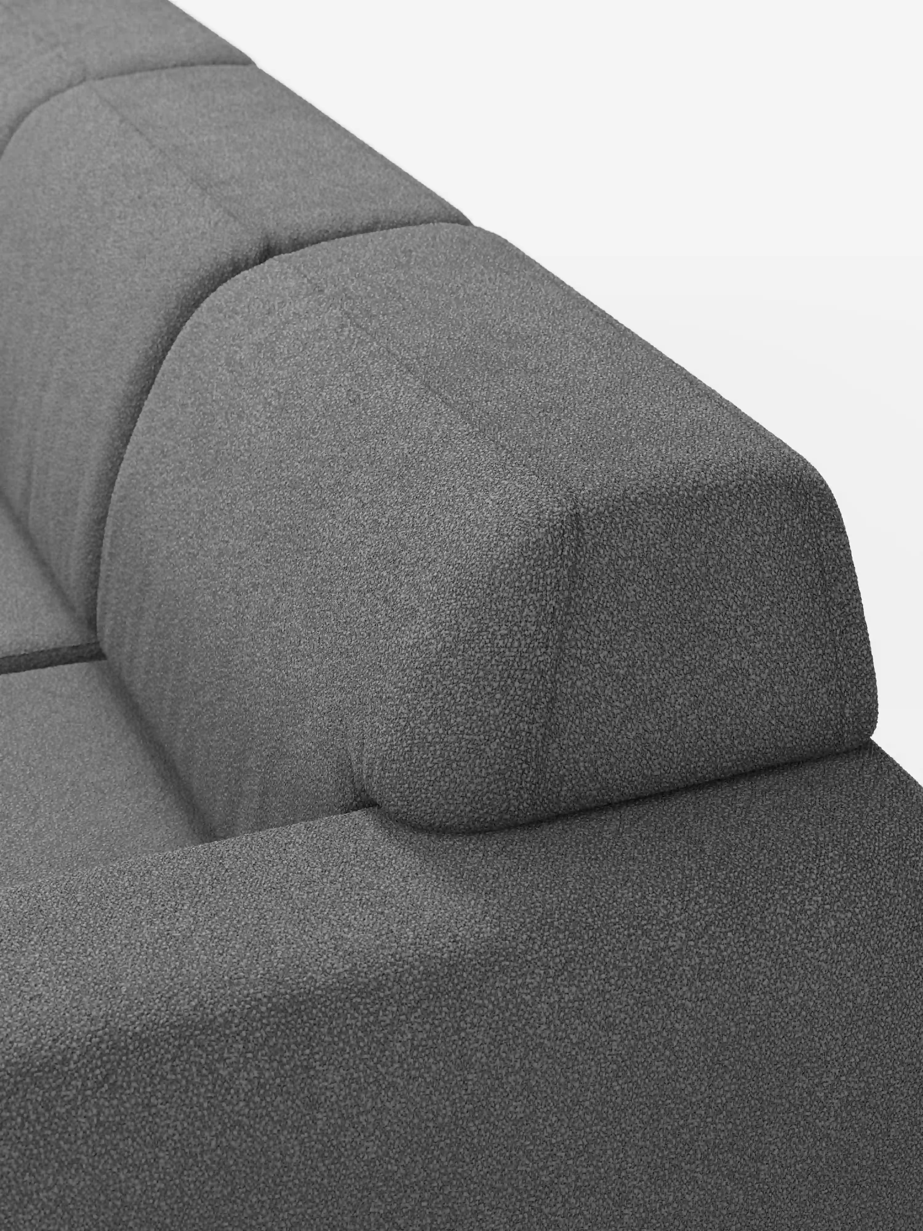 Primo piano del divano angolare Orbit con penisola reversibile e tutte le sedute allungabili in tessuto smacchiabile effetto cotone T33 di Divani.Store, caratterizzato da un moderno rivestimento grigio con schienale e braccioli dalla forma geometrica a blocchi. Su uno sfondo bianco, il tessuto a trama fitta effetto cotone e le linee pulite e dritte mettono in risalto la raffinata eleganza tipica dei divani di alta gamma.