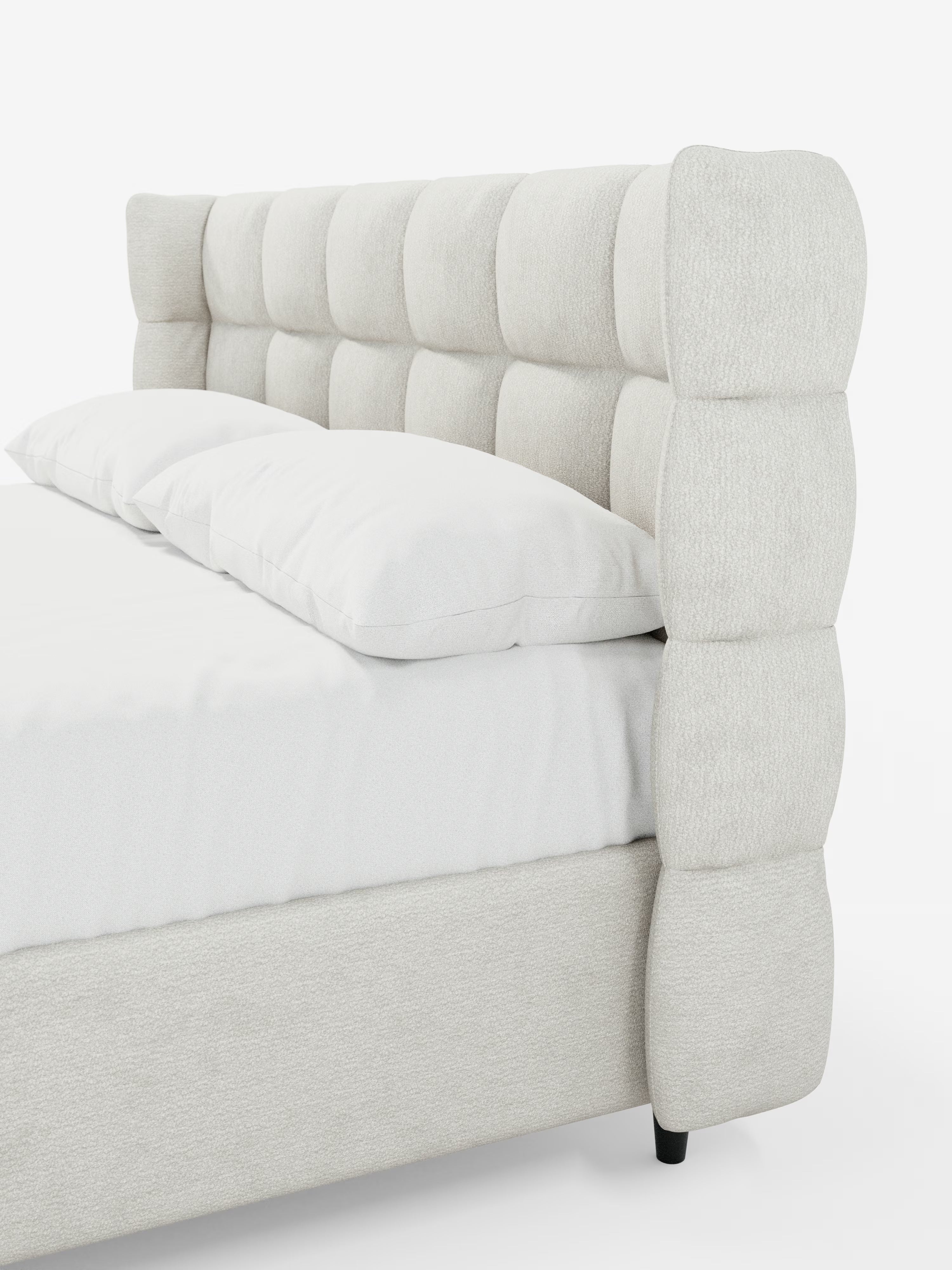 Un primo piano del letto imbottito RAGNAR con contenitore e testiera capitonné avvolgente di Letti.store, qui presentato in un moderno tessuto beige chiaro certificato Oeko-Tex®. L’alta testiera avvolgente presenta un’elegante griglia di morbidi quadrati imbottiti, mentre il letto è rifatto con cura con un lenzuolo bianco e un unico cuscino lungo.