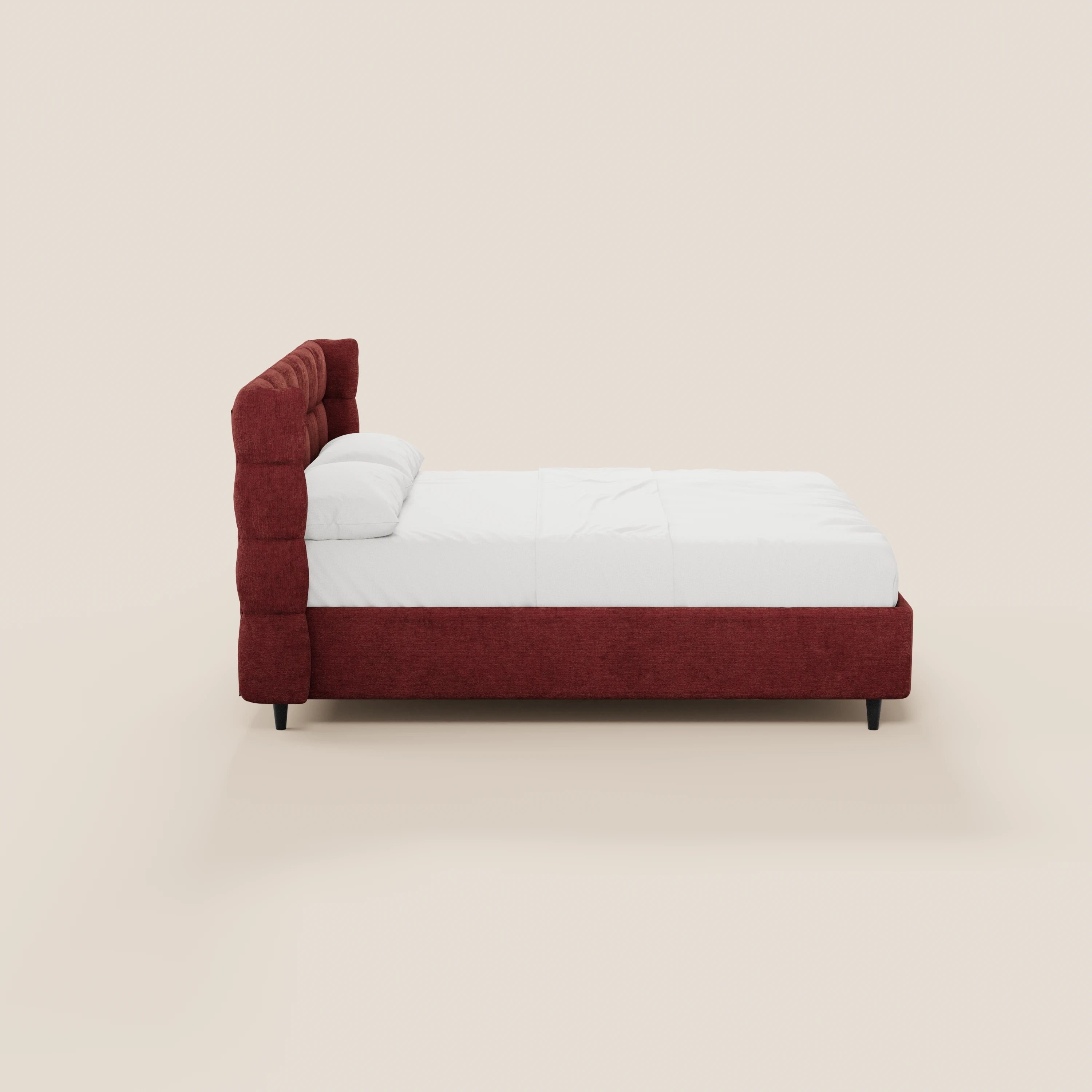 Una vista laterale del letto imbottito RAGNAR con contenitore e testiera capitonné avvolgente di Letti.store, realizzato in un elegante tessuto rosso certificato Oeko-Tex®, con lenzuola e cuscini bianchi, su uno sfondo beige chiaro.