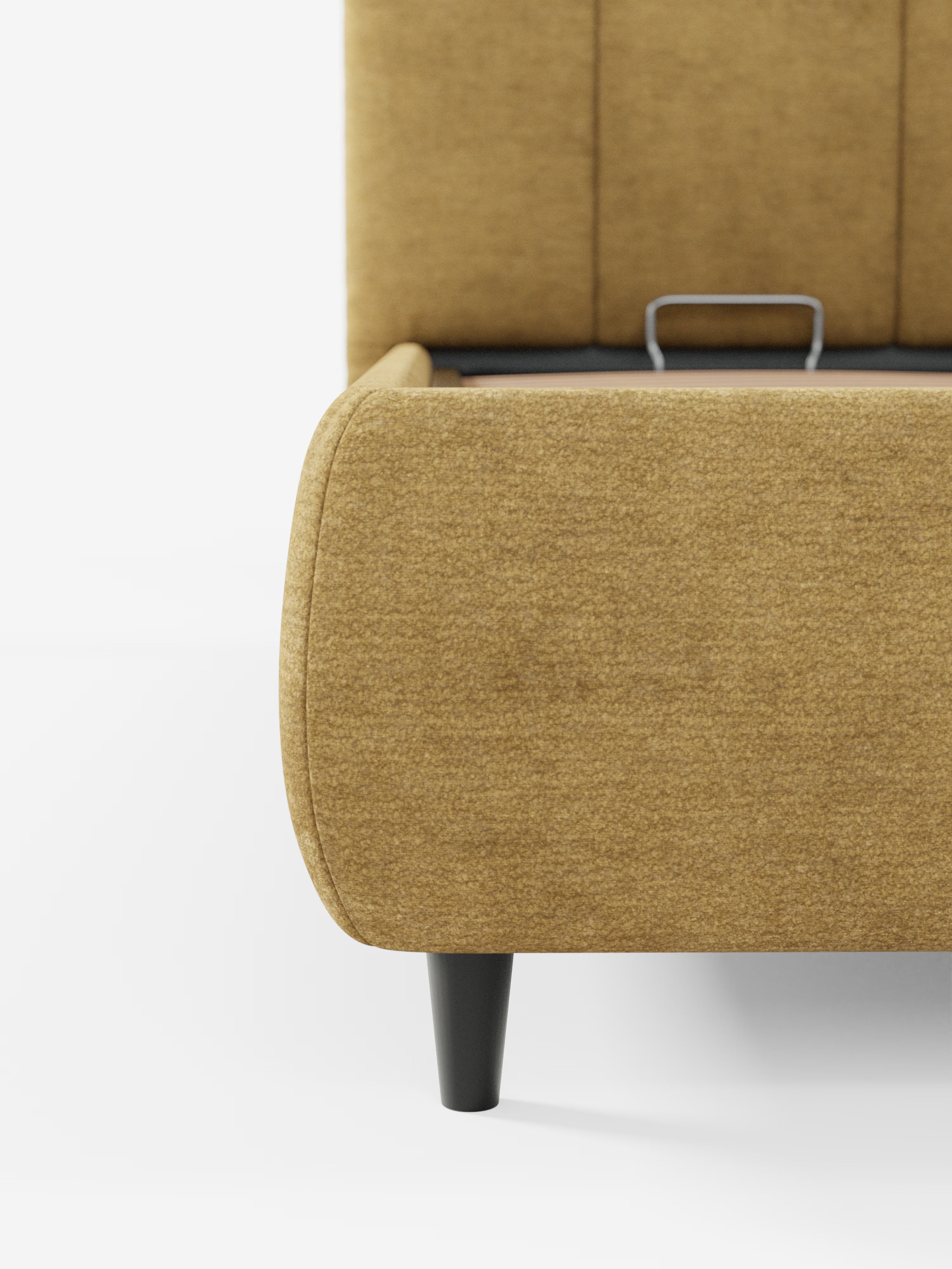 Un primo piano del letto imbottito ARKAM con contenitore e testiera a lavorazione verticale di Letti.store, qui presentato in un tessuto giallo senape certificato Oeko-Tex®. La struttura del letto presenta bordi arrotondati, gambe affusolate nere e lascia intravedere il supporto metallico per il materasso all’interno. La testiera imbottita con cuciture verticali esalta il comfort e contribuisce al suo design shabby chic, mentre lo sfondo bianco crea un’estetica pulita e minimalista.