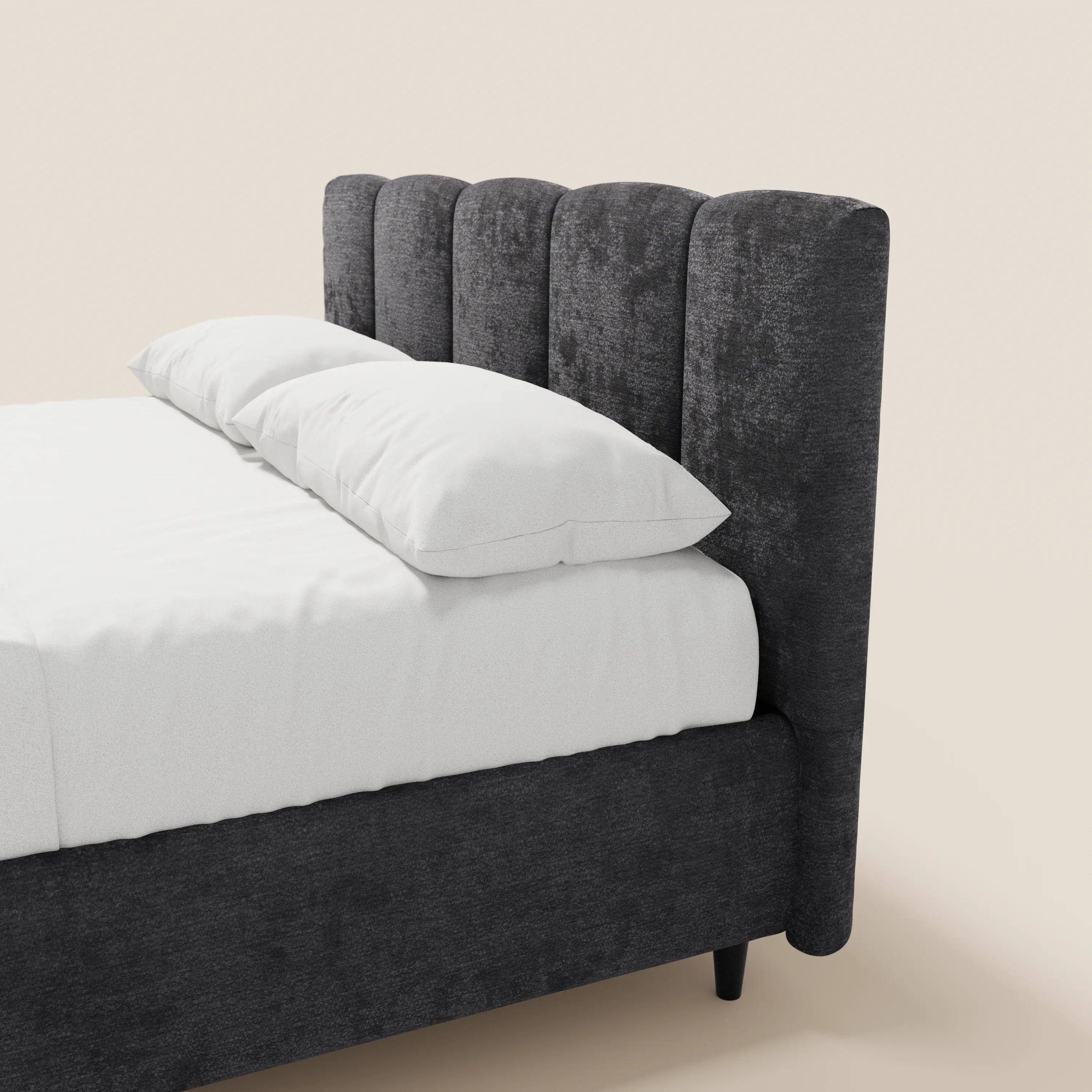 Una vista parziale del letto imbottito ARKAM con contenitore di Letti.store: design shabby chic con testiera in tessuto Oeko-Tex® cucito verticalmente, biancheria da letto bianca e due cuscini sovrapposti su uno sfondo beige chiaro a tinta unita.
