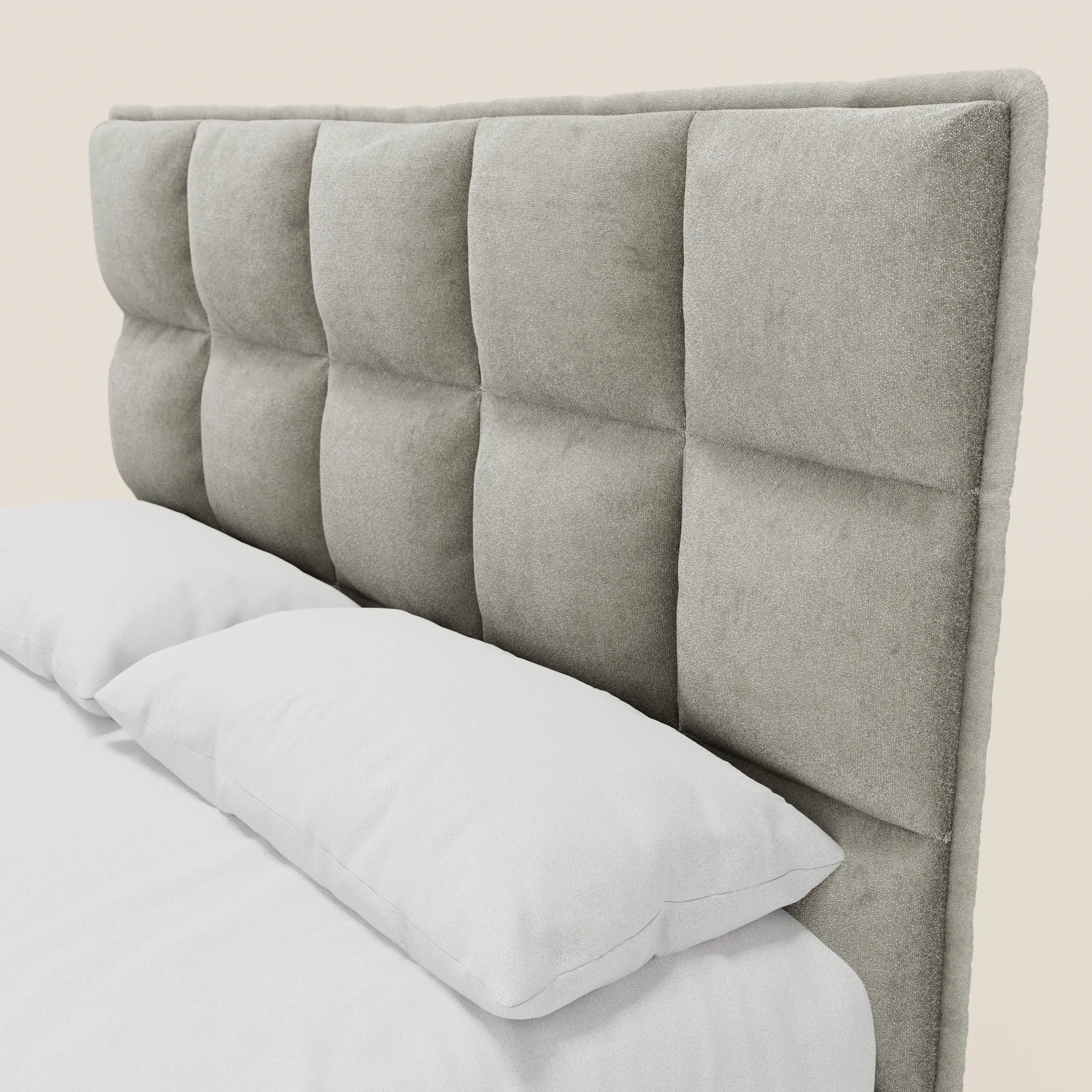 Un primo piano del letto imbottito AURO con contenitore e testiera capitonné alta in ciniglia Oeko-Tex® di Letti.store mette in risalto la sua ampia testiera capitonné di colore grigio chiaro. La biancheria da letto di un bianco brillante esalta il fascino moderno e neutro del letto.