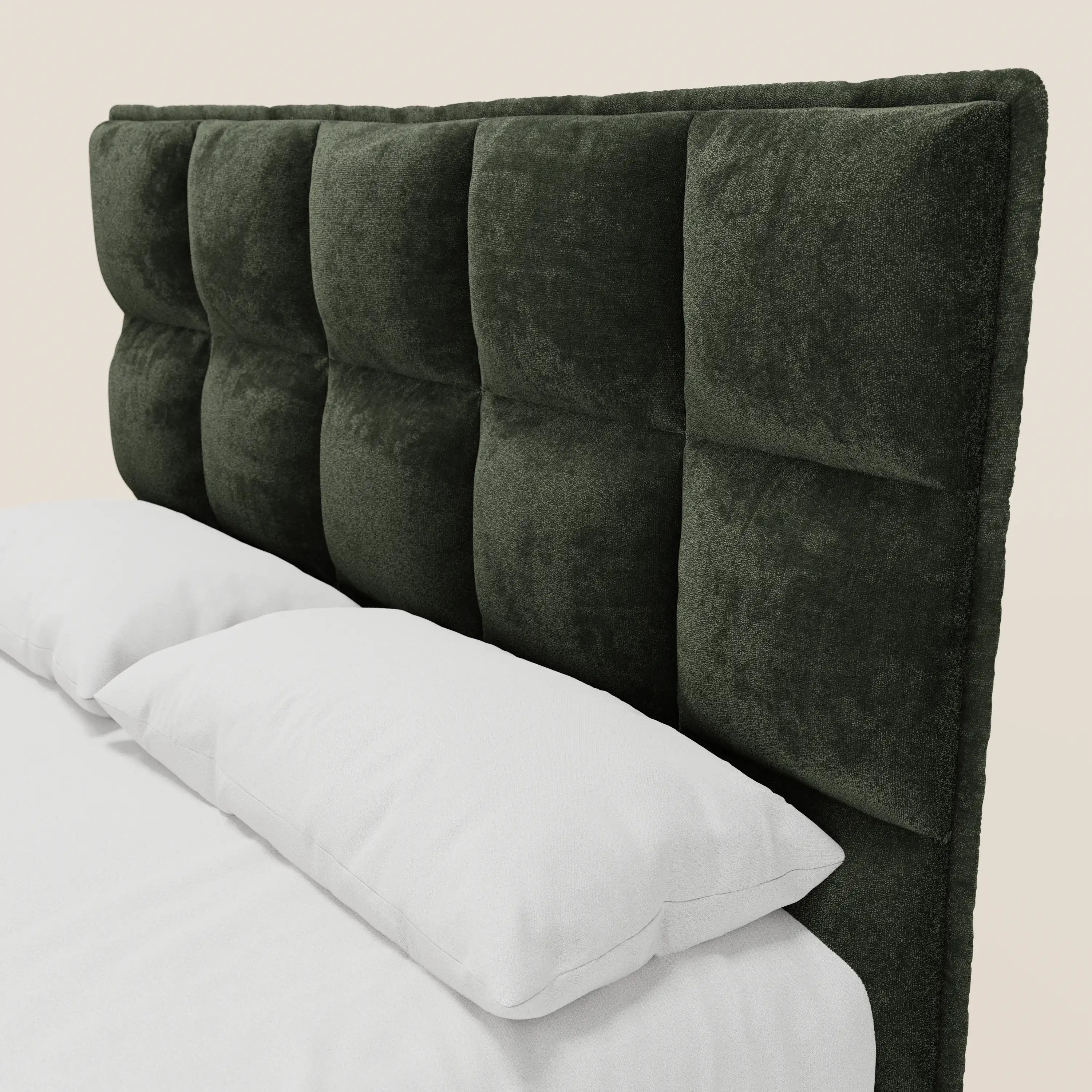 Un primo piano del modello AURO di Letti.store mette in risalto la sua testiera alta in ciniglia capitonné verde scuro certificata Oeko-Tex®, con quadrati trapuntati. Il letto è caratterizzato da biancheria da letto di un bianco candido e da una base contenitiva, il tutto su uno sfondo beige chiaro.