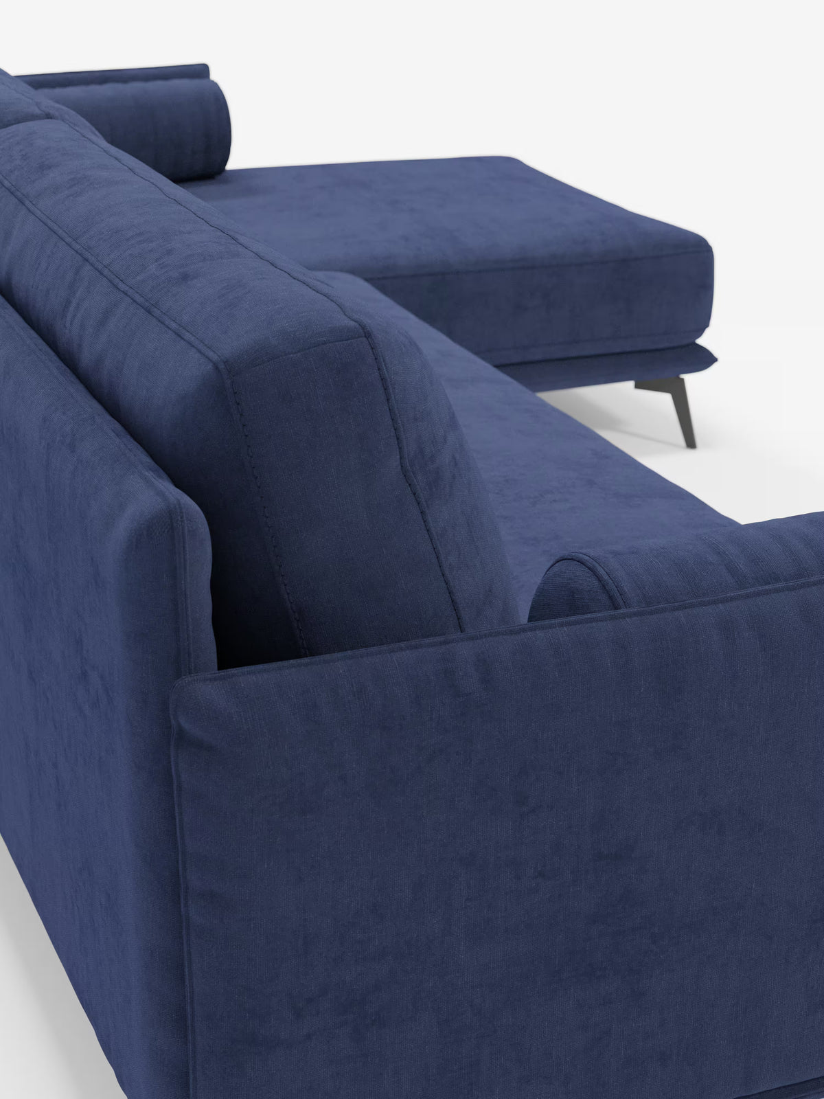 Primo piano del divano moderno angolare con penisola “Basalto” di Divani.Store, rivestito in tessuto T31 blu scuro e resistente alle macchie. Questo elegante divano componibile presenta ampi braccioli rettangolari, morbidi cuscini in piuma e una robusta base in metallo con sottili gambe nere inclinate. La chaise longue si estende verso destra e due cuscini cilindrici completano il design raffinato di questo divano contemporaneo.