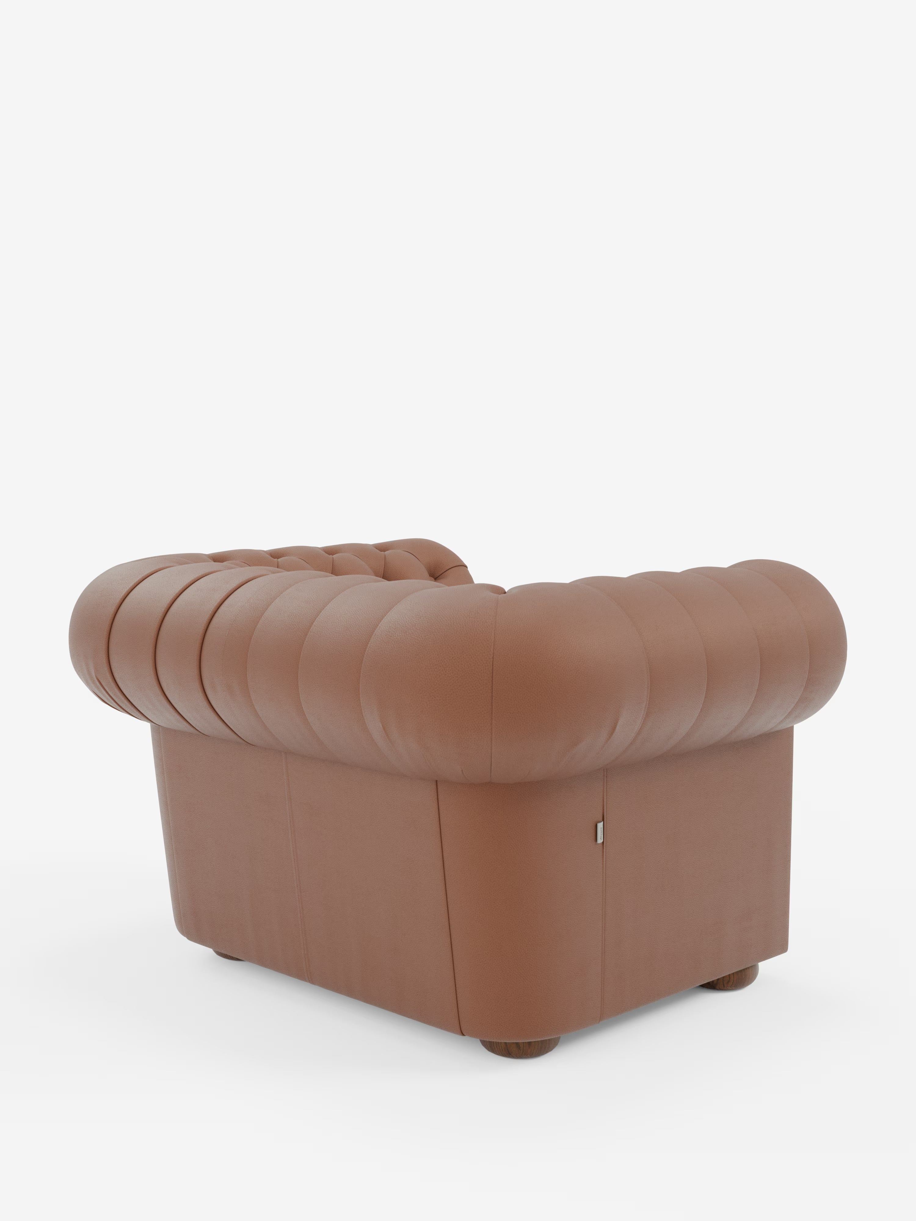 Una poltrona Chester in vera pelle spessorata con capitonné artigianale di Divani.Store: questa poltrona in pelle marrone presenta una profonda trapuntatura realizzata a mano e bordi arrotondati. Vista dal lato posteriore sinistro, mostra una base squadrata, piedini corti e rotondi in legno e un'imbottitura morbida e soffice. Lo sfondo è bianco a tinta unita.