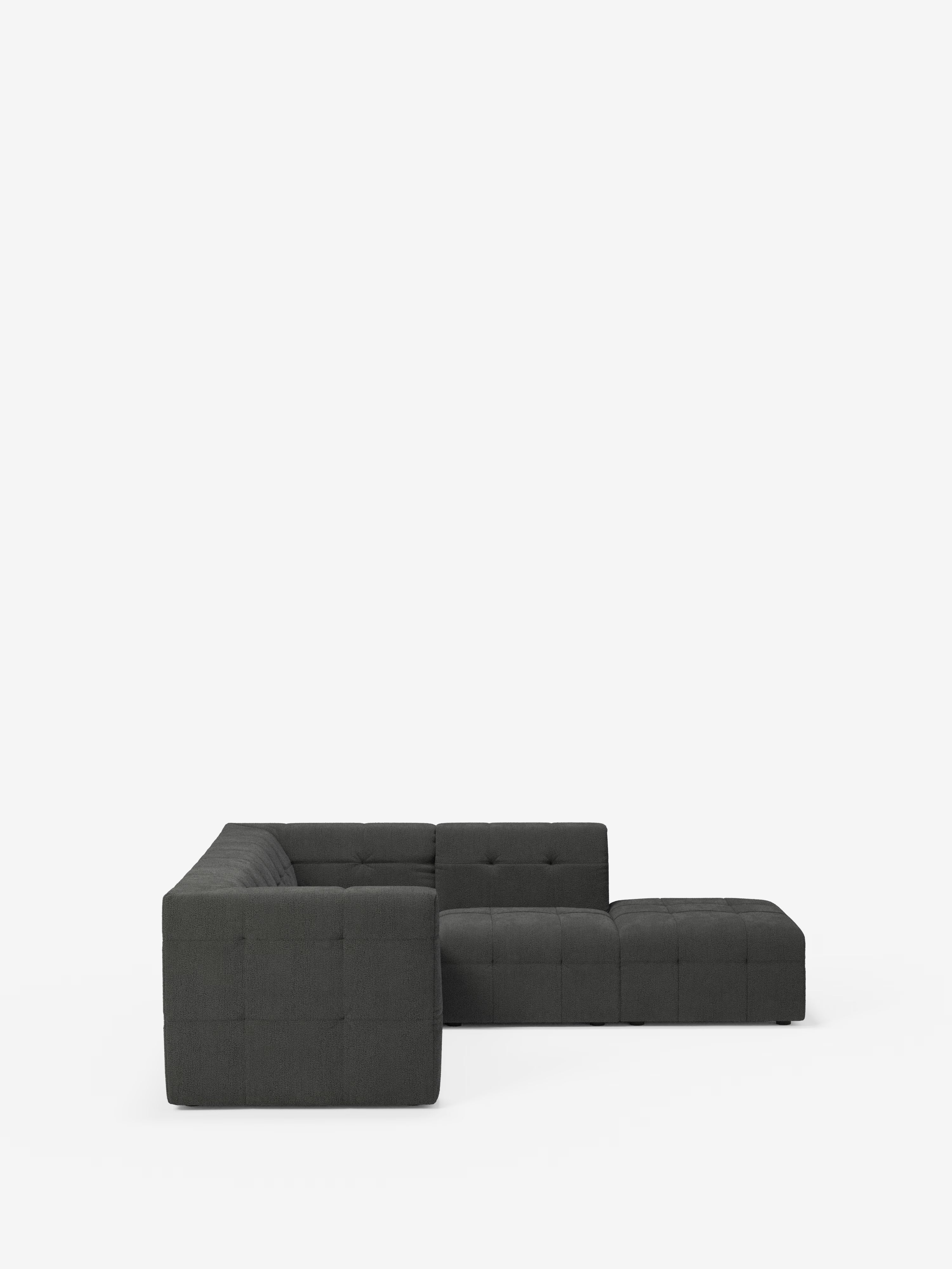 Un moderno divano angolare componibile e modulare Mosaic a forma di L in bouclé di Divani.Store, rivestito in tessuto T21 grigio scuro smacchiabile con motivo capitonné, si staglia su uno sfondo bianco. Il divano componibile presenta un bracciolo sinistro e due moduli pouf che si estendono verso l’esterno, creando una spaziosa zona salotto dalle linee pulite e minimaliste, perfetta per qualsiasi soggiorno moderno.