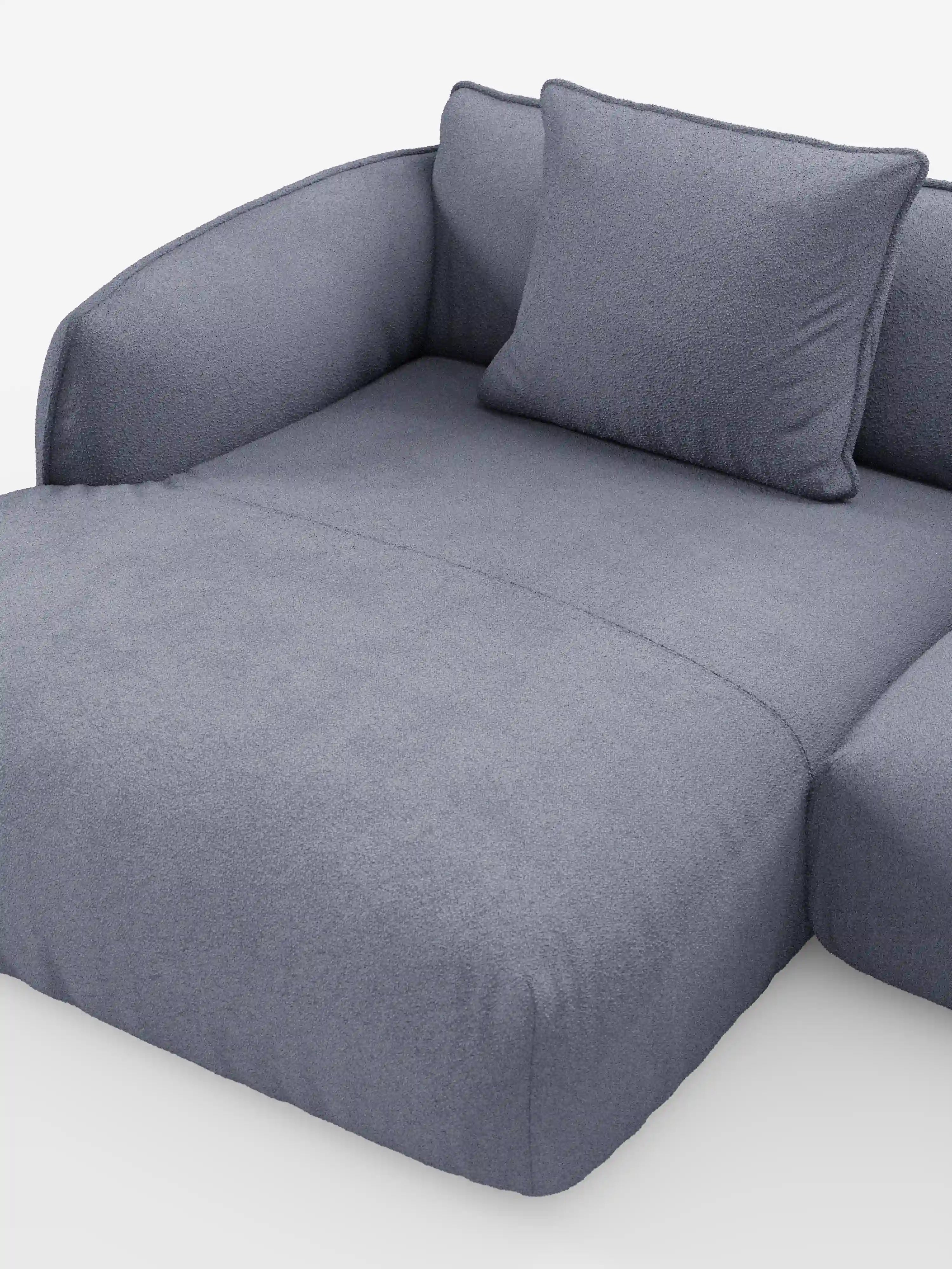 Un divano angolare panoramico componibile Nimbus in stile contemporaneo con penisola e angolo in tessuto antimacchia T33 di Divani.Store, rivestito in morbido tessuto grigio chiaro antimacchia, caratterizzato da braccioli arrotondati e da un cuscino quadrato coordinato. Il morbido tessuto della poltrona avvolge l’intera struttura, conferendole un aspetto accogliente e invitante senza gambe o base a vista, in linea con lo stile elegante dei moderni divani componibili.