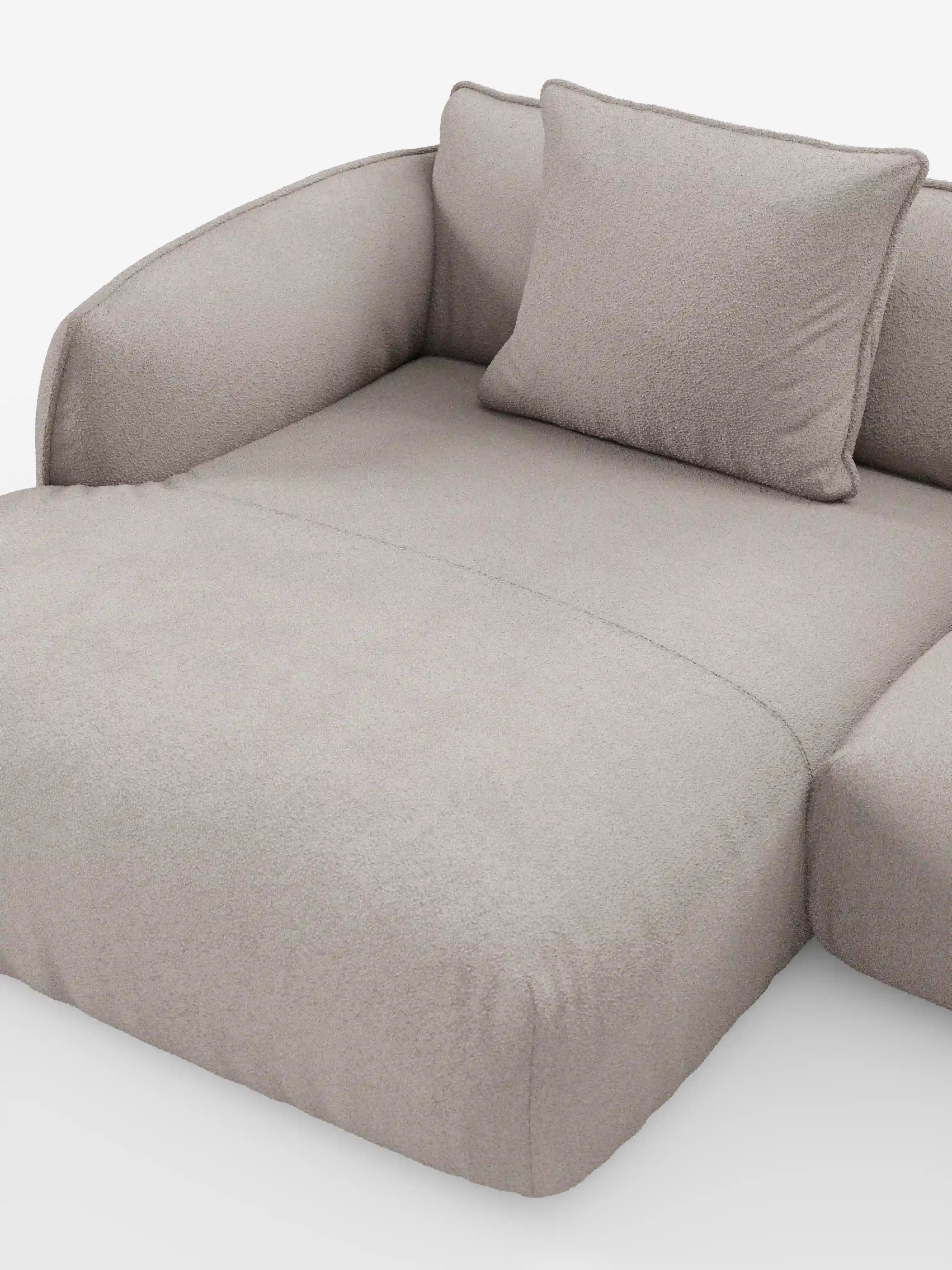Un divano angolare panoramico componibile Nimbus in stile contemporaneo con penisola e angolo in tessuto smacchiabile T33 di Divani.Store, rivestito in tessuto beige chiaro con una finitura morbida e testurizzata. Questo divano Made in Italy presenta sedute profonde, braccioli arrotondati ed è corredato da un unico cuscino quadrato coordinato, il tutto presentato su uno sfondo bianco a tinta unita.